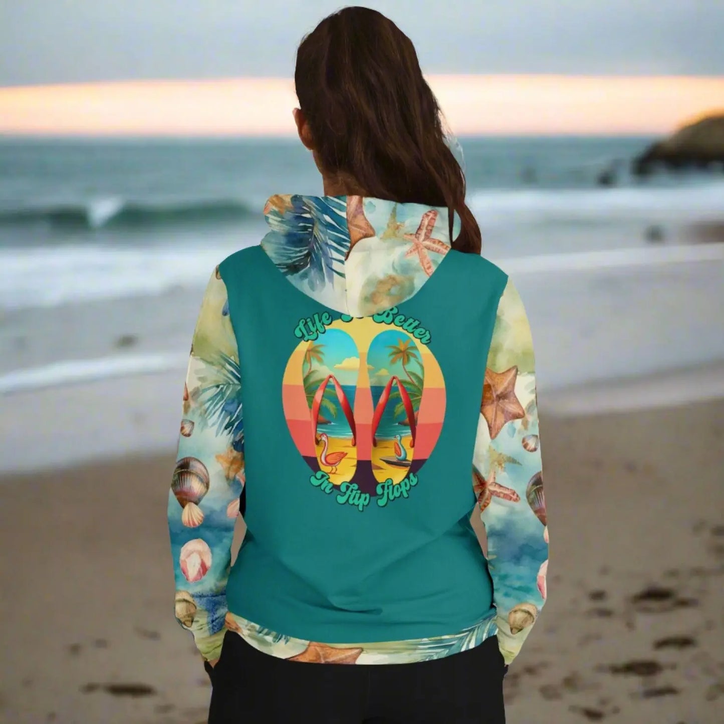 Back view of woman in sweatshirt with teal back with seashell patterned sleeves and hood Life is better in flip flops with graphic of beach scene flip flops.