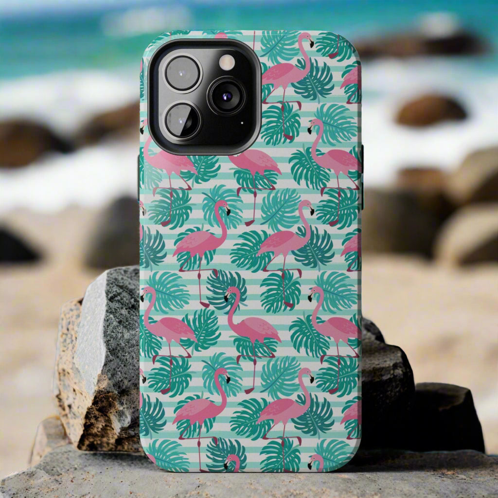 Phone case with flamingo and leaf pattern laying against rocks at the beach.