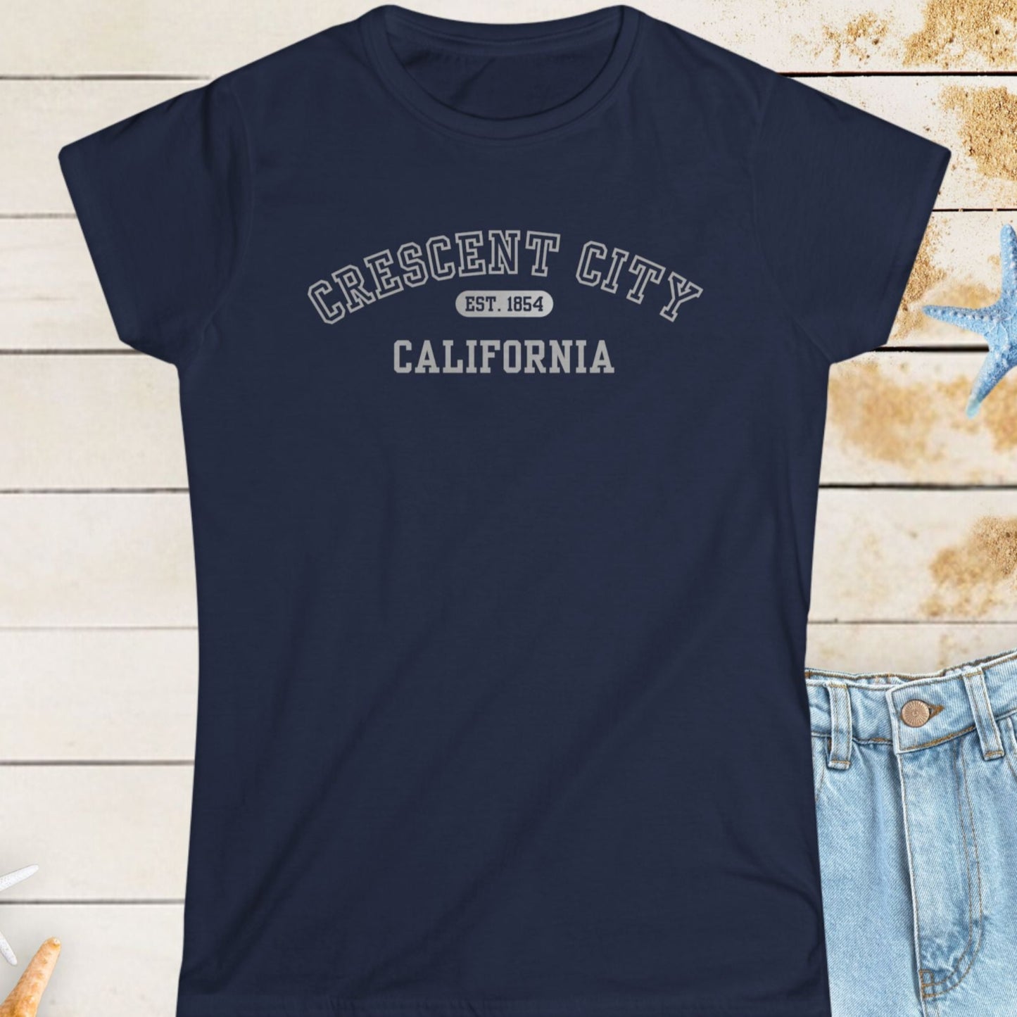 Navy blue t-shirt with 'Crescent City, California' text on a wooden surface with starfish.