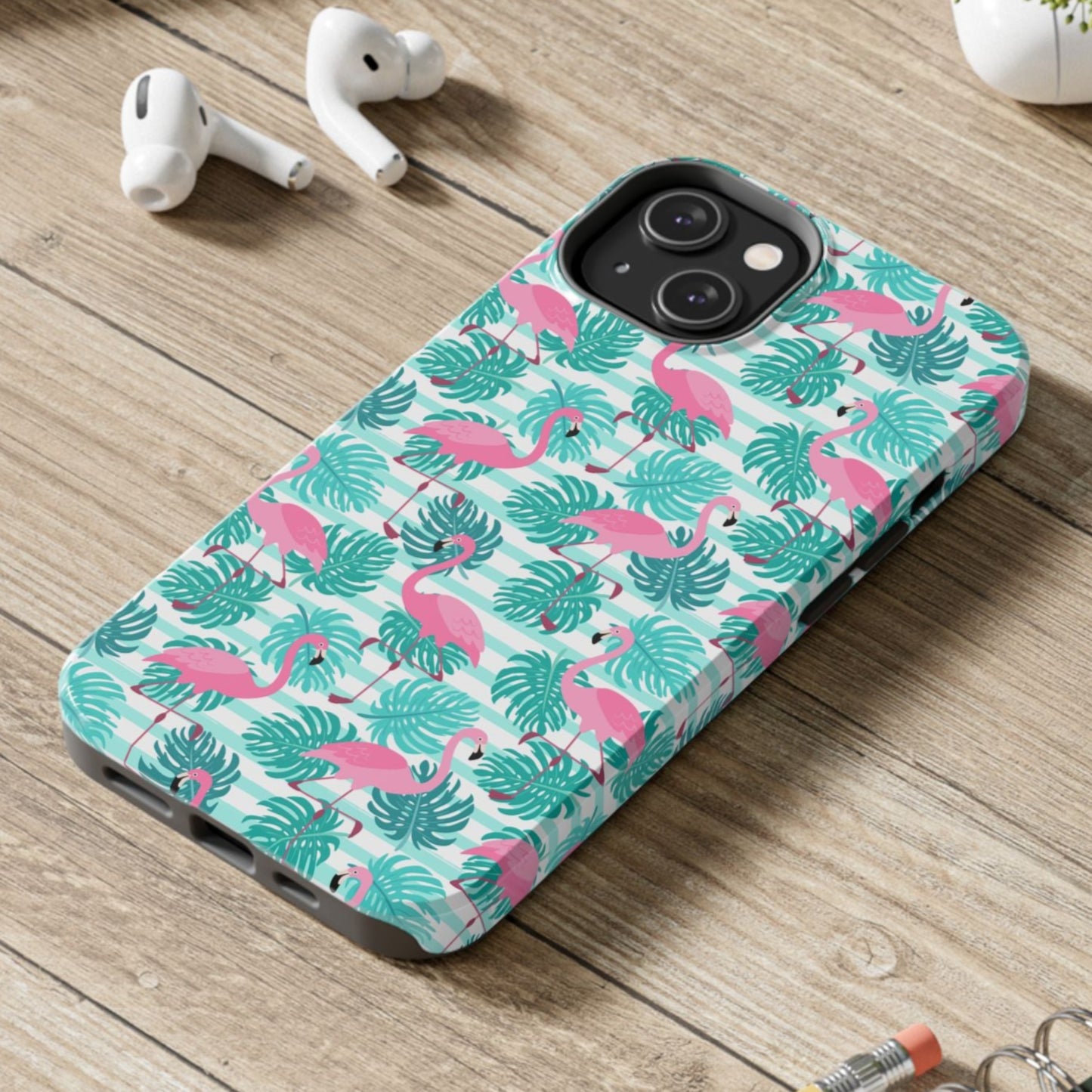 Phone case with flamingo and leaf pattern on a wooden surface with laptop, earbuds, and notebook.