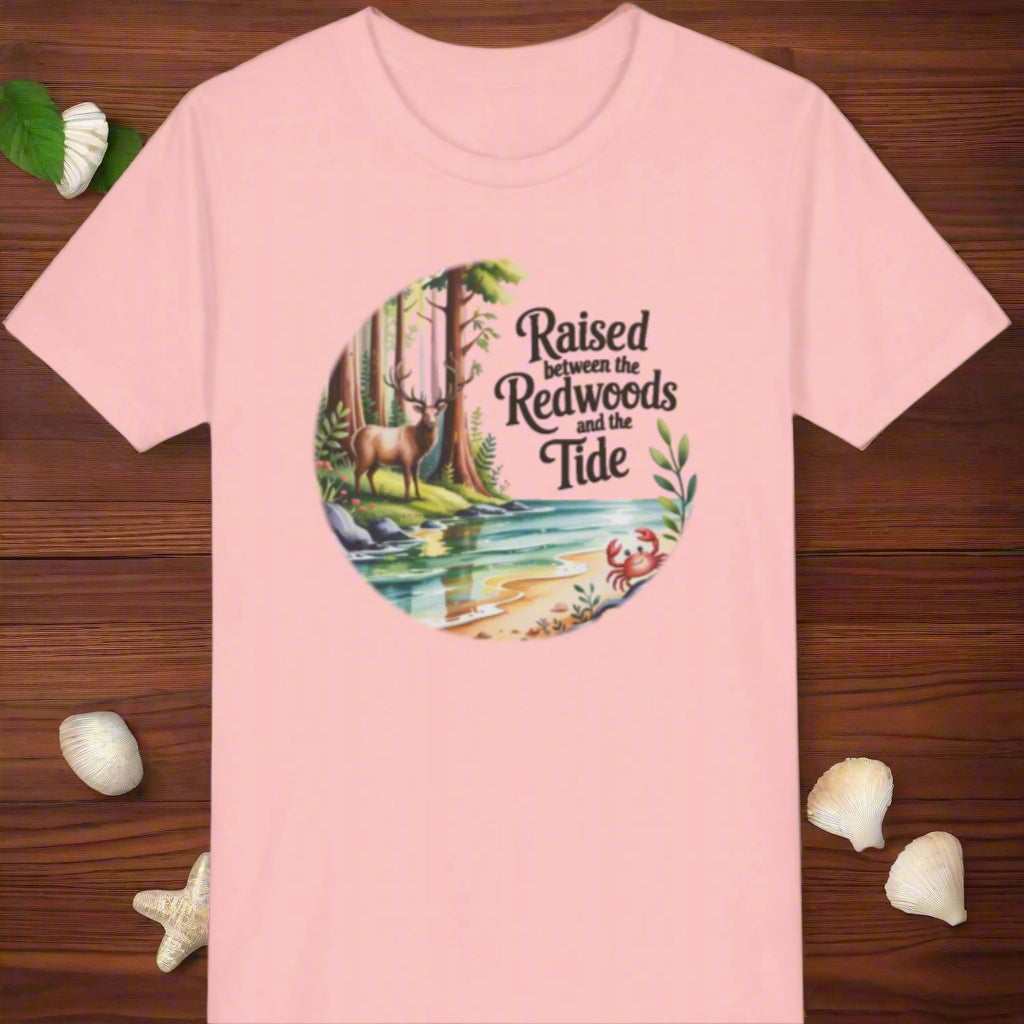 Pink t-shirt with nature-themed graphic and text 'Raised between the Redwoods and the Tide'.