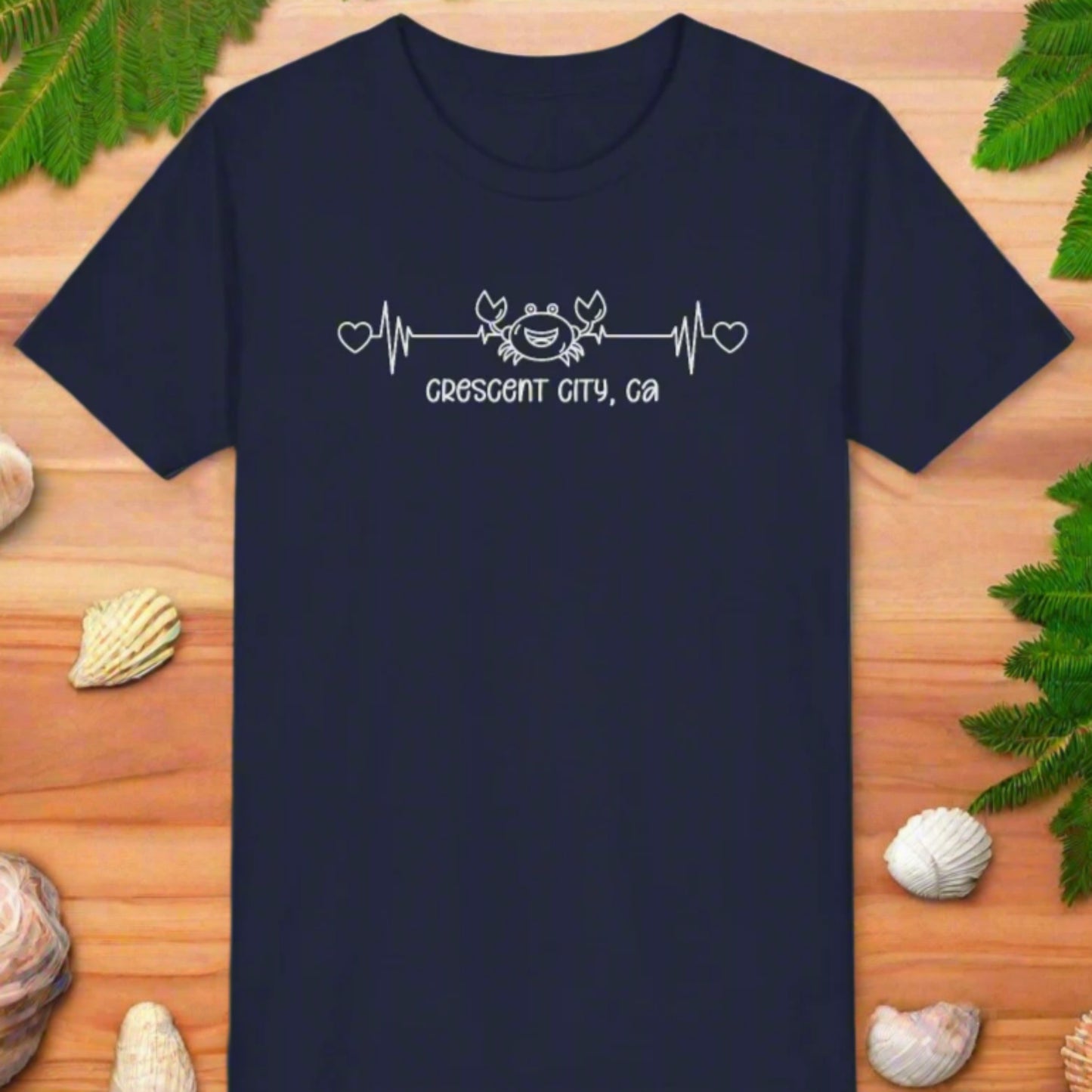 Navy Child t-shirt with a smiley crab on a heartbeat line with hearts at both ends and “Crescent City, CA” underneath the design.