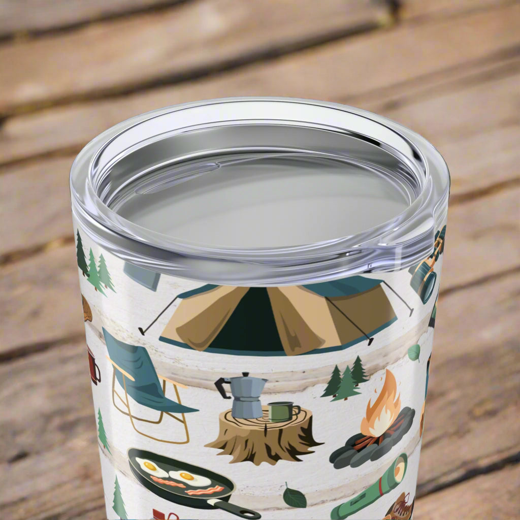 Top view of 20oz tumbler with light wood background and repeating pattern of hiking boots, tents, campfires, flashlights, maps, and backpacks; glossy finish with secure lid.