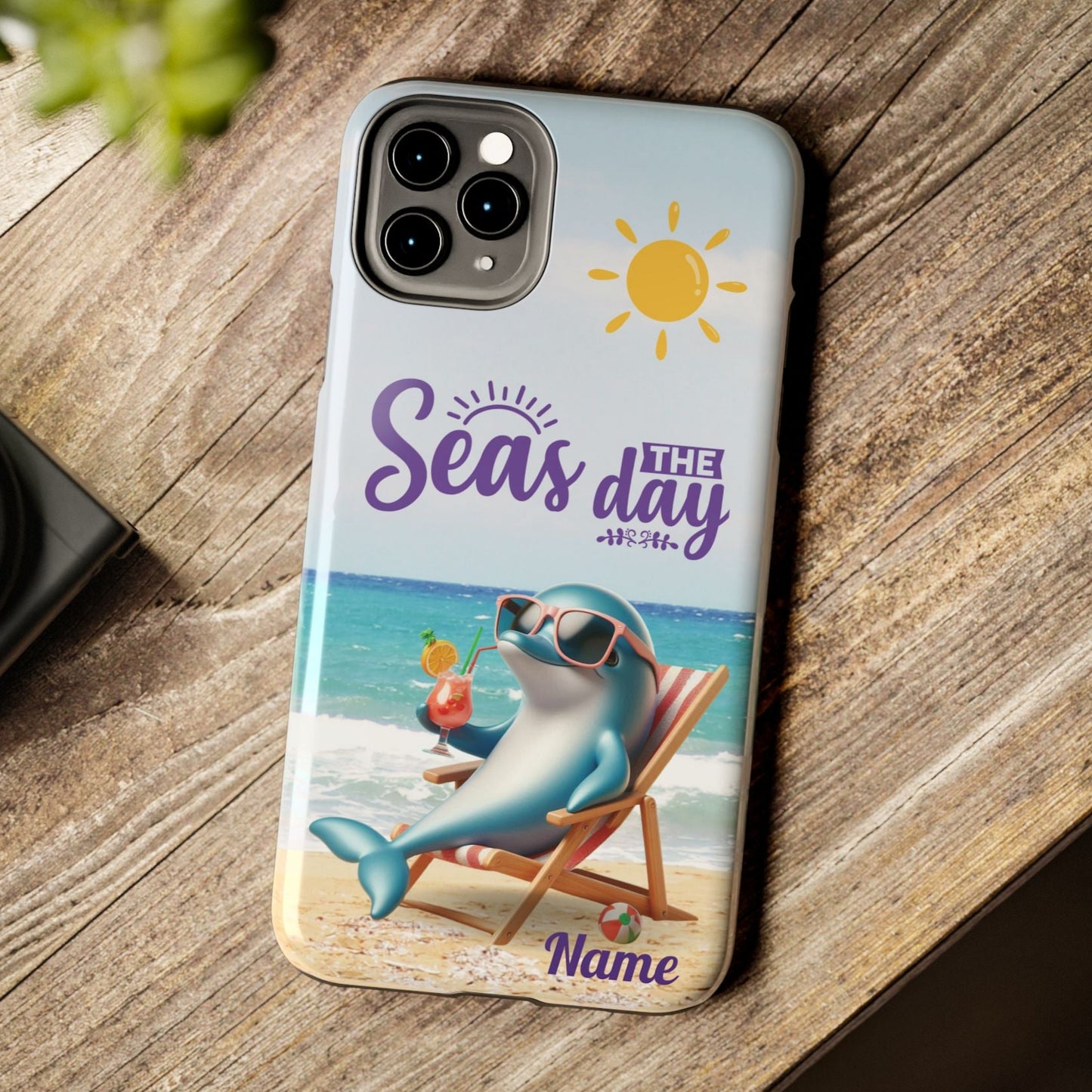 Seas the Day dolphin-themed phone case with personalized name, glossy finish, and beach-inspired design with a dolphin enjoying a cocktail during a sunny day on the beach with the phrase Seas the Day.