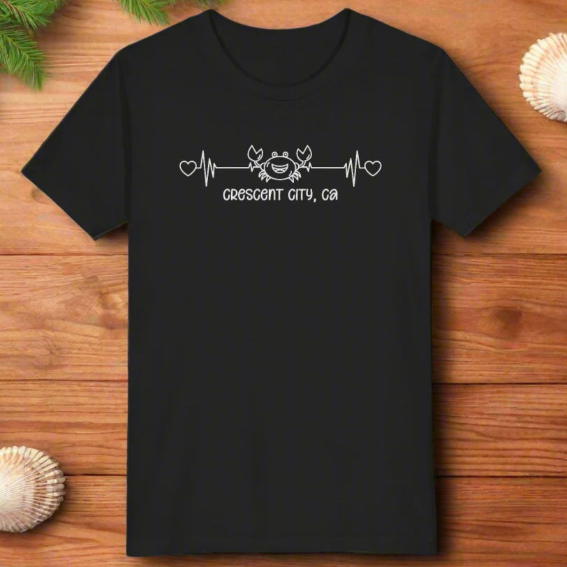 Black Child t-shirt with a smiley crab on a heartbeat line with hearts at both ends and “Crescent City, CA” underneath the design.