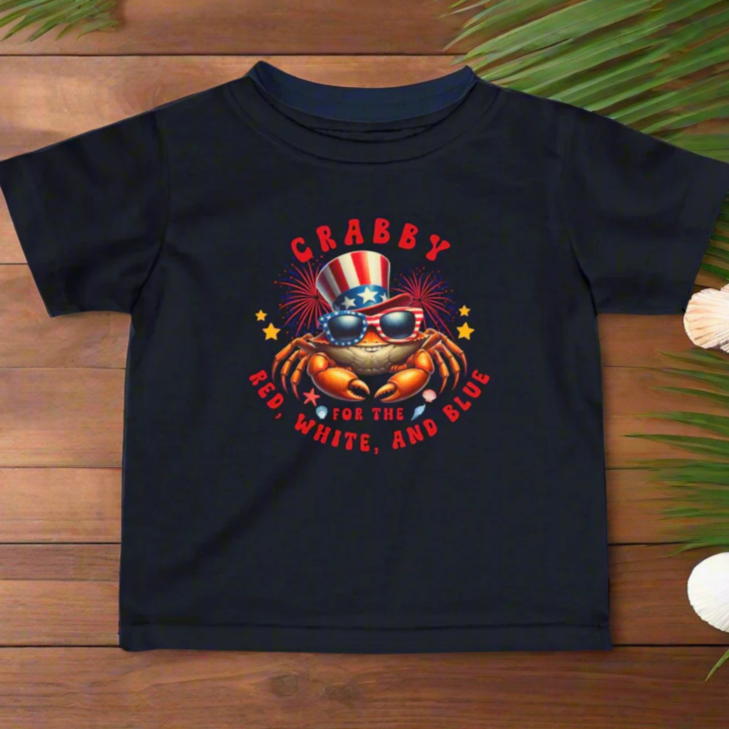 Navy Infant t-shirt with a crab wearing an American flag top hat surrounded by fireworks and seashells with the phrase “Crabby for the Red, White, and Blue.”