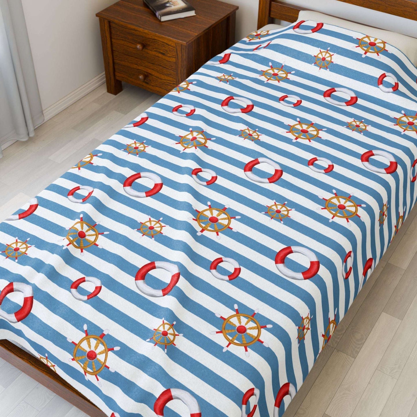 Bed with a nautical-themed velveteen blanket featuring blue stripes, red life buoys, and ship wheels.