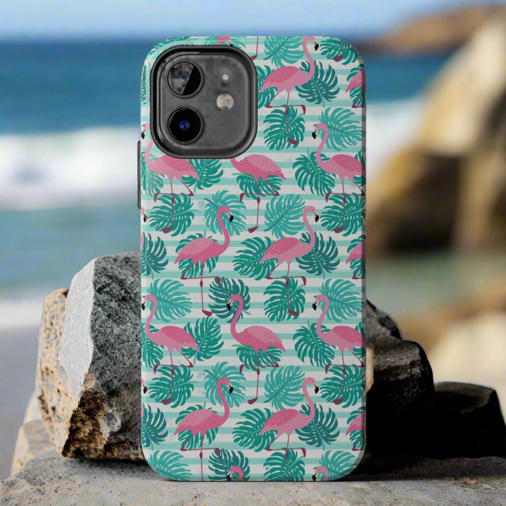 Phone case with flamingo and leaf pattern laying against rocks at the beach.