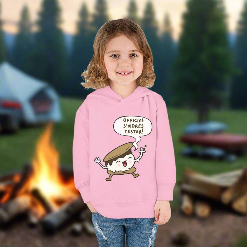 Girl wearing pink cozy toddler hoodie with “Official S’mores Tester” speech bubble and a cartoon s'more – cute outdoor-themed sweatshirt for little campers.