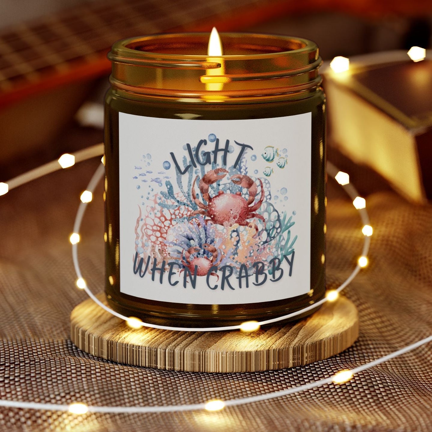 Candle in a jar with a decorative label on a wooden coaster, surrounded by string lights and a guitar in the background.
