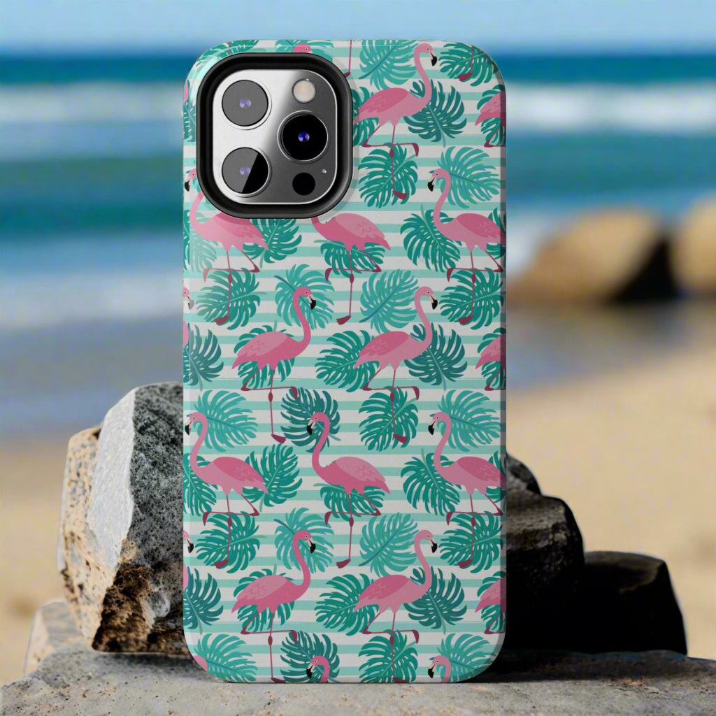 Phone case with flamingo and leaf pattern laying against rocks at the beach.