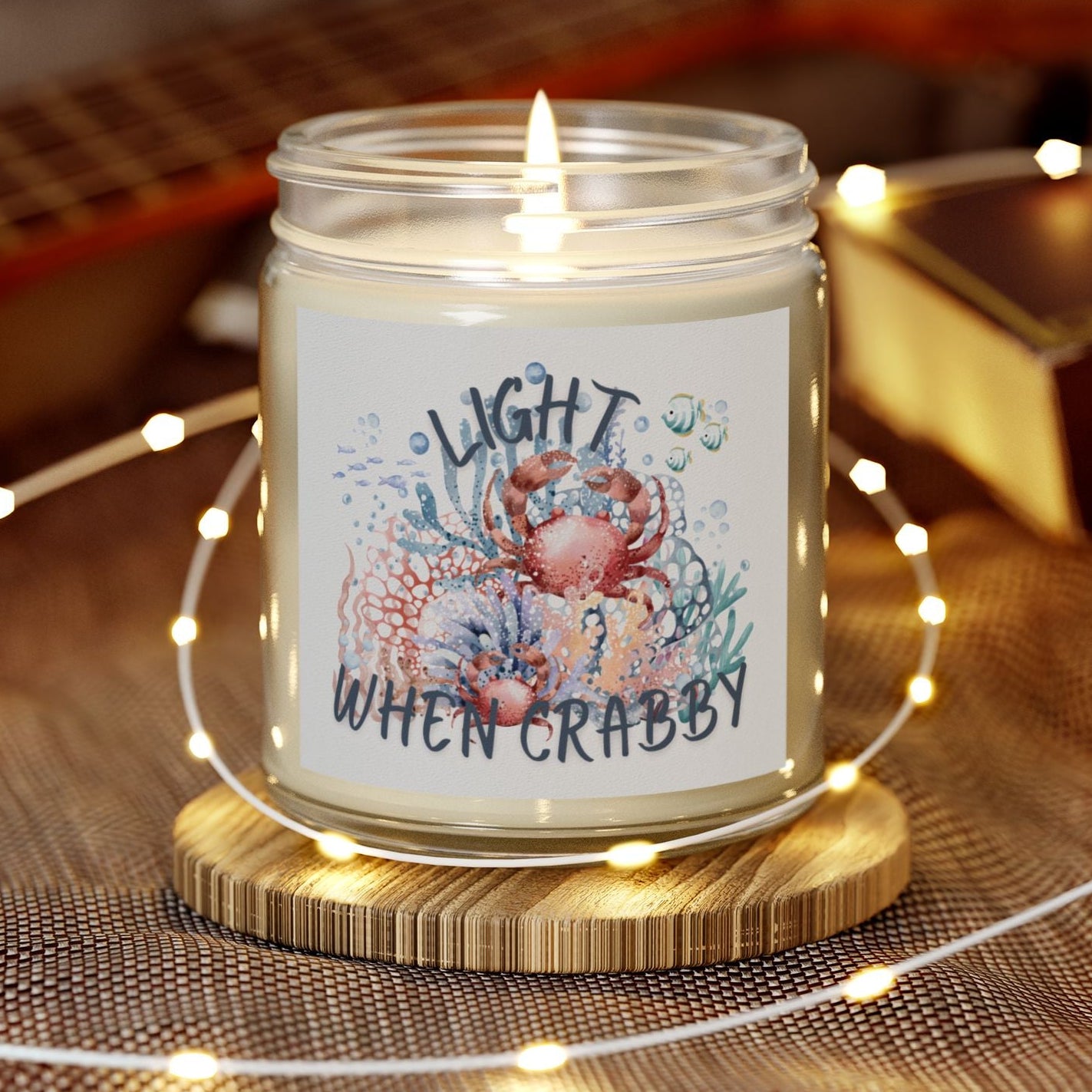 Candle in a jar with a decorative label on a wooden coaster, surrounded by string lights and a guitar in the background.