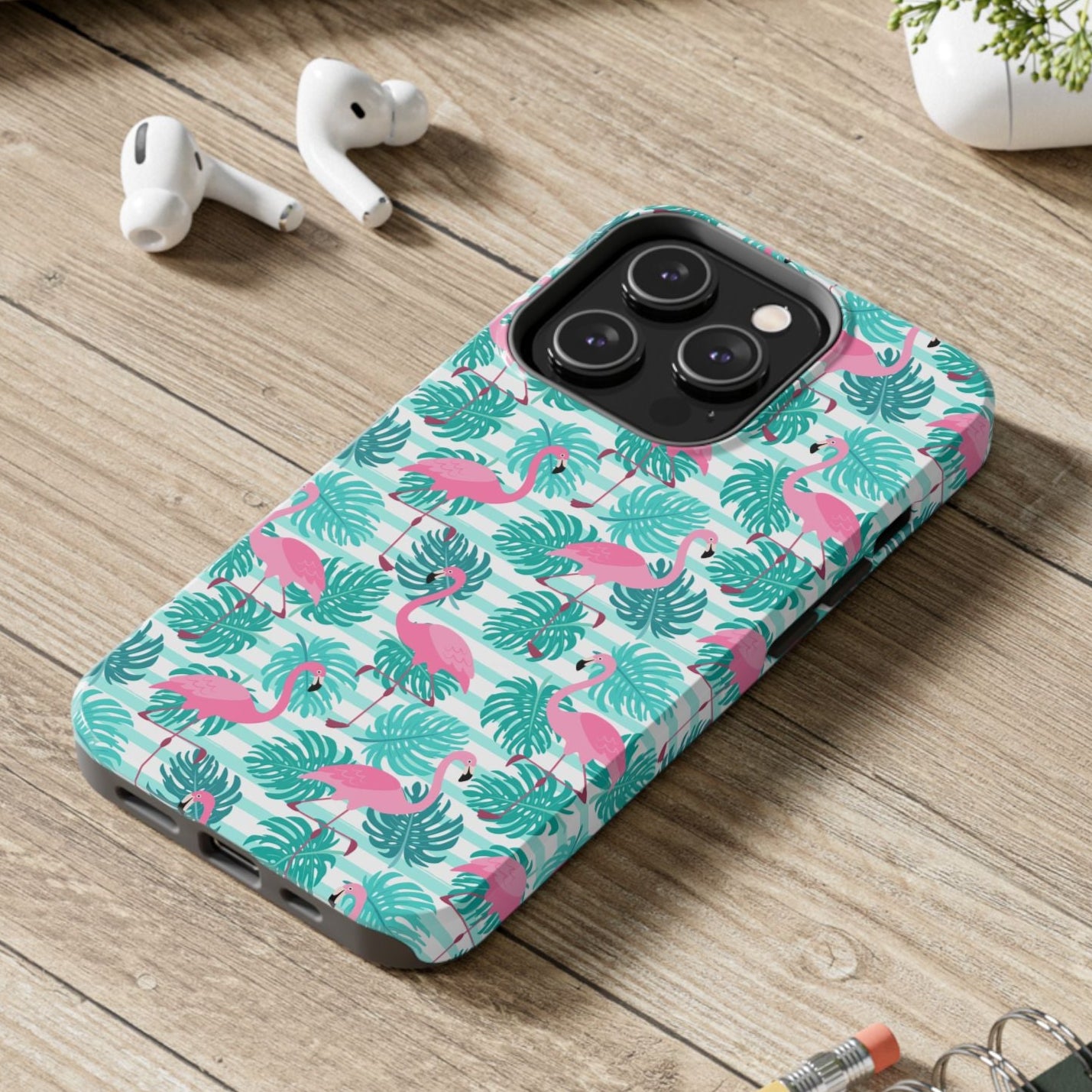 Phone case with flamingo pattern on a wooden surface with laptop, earbuds, and notebook.