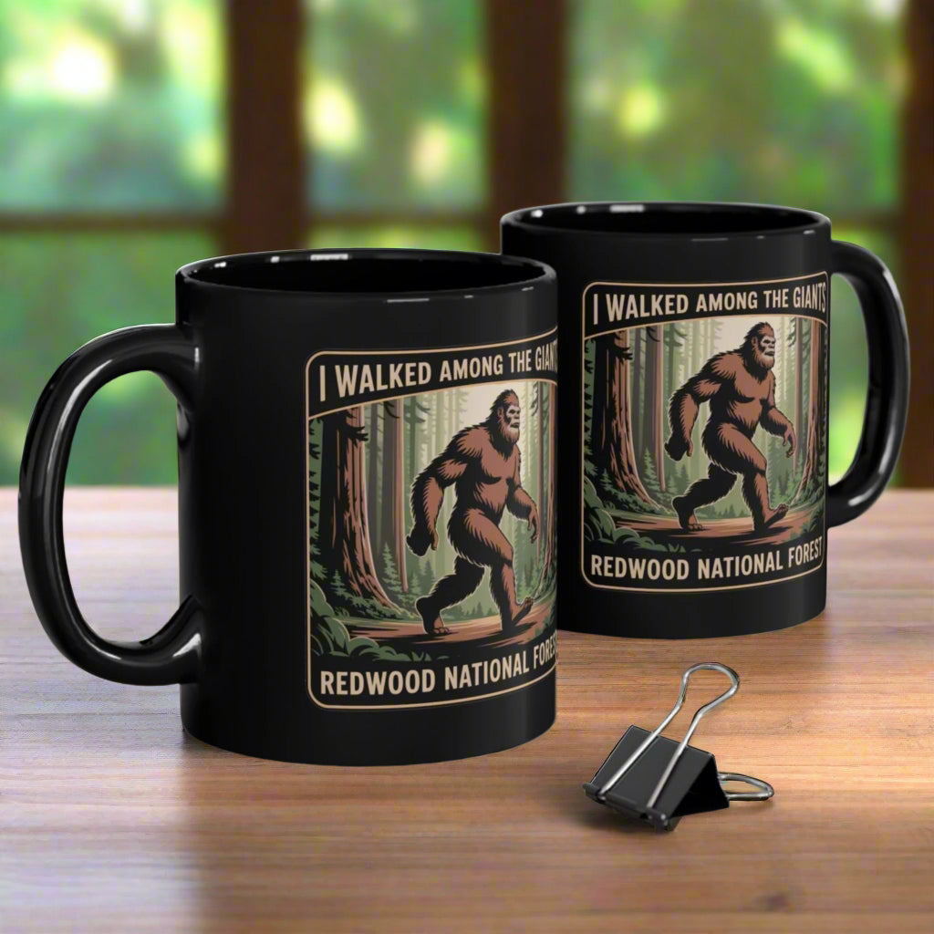 Two black mugs with Bigfoot design and text on a wooden surface.