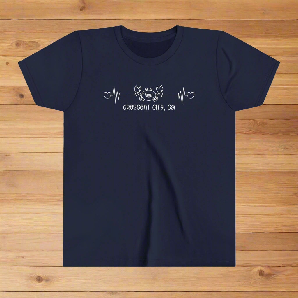 Navy Youth t-shirt with a smiley crab on a heartbeat line with hearts at both ends and “Crescent City, CA” underneath the design.