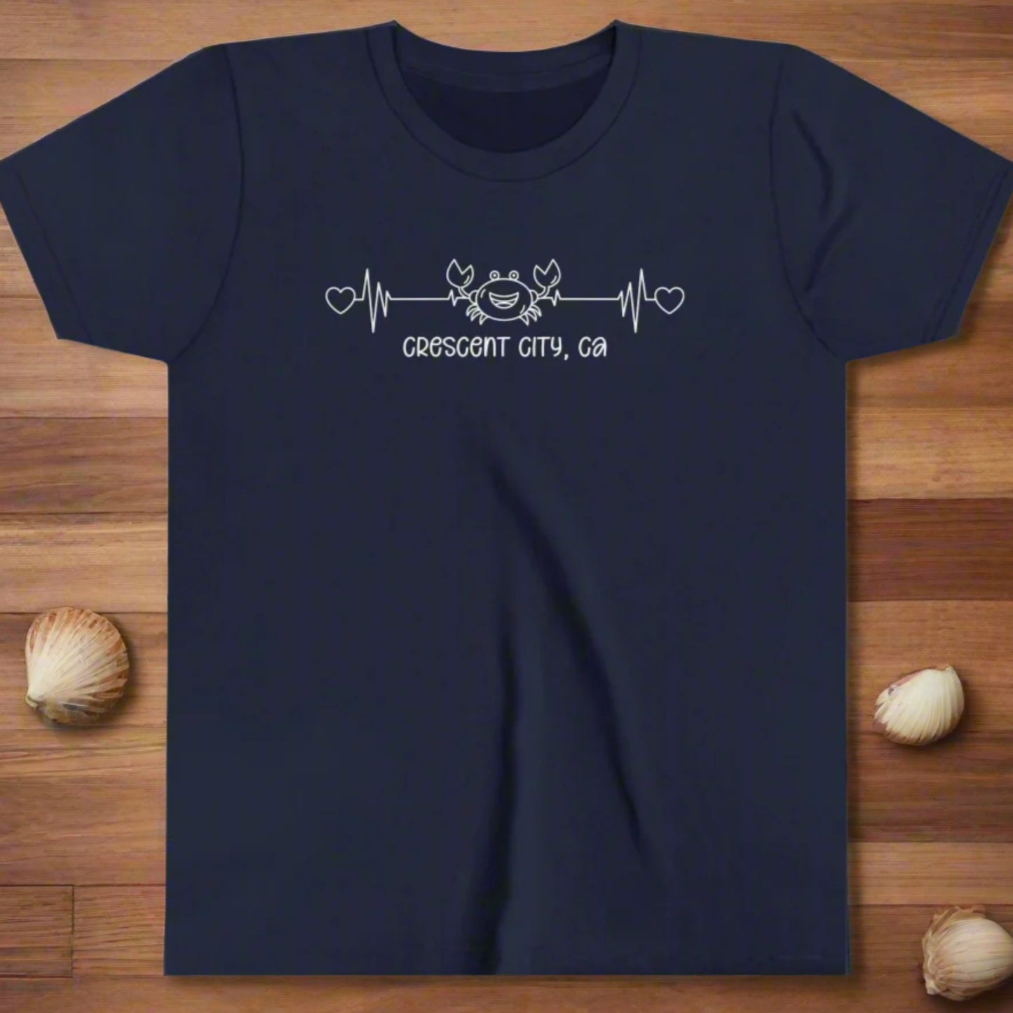 Navy Youth t-shirt with a smiley crab on a heartbeat line with hearts at both ends and “Crescent City, CA” underneath the design.