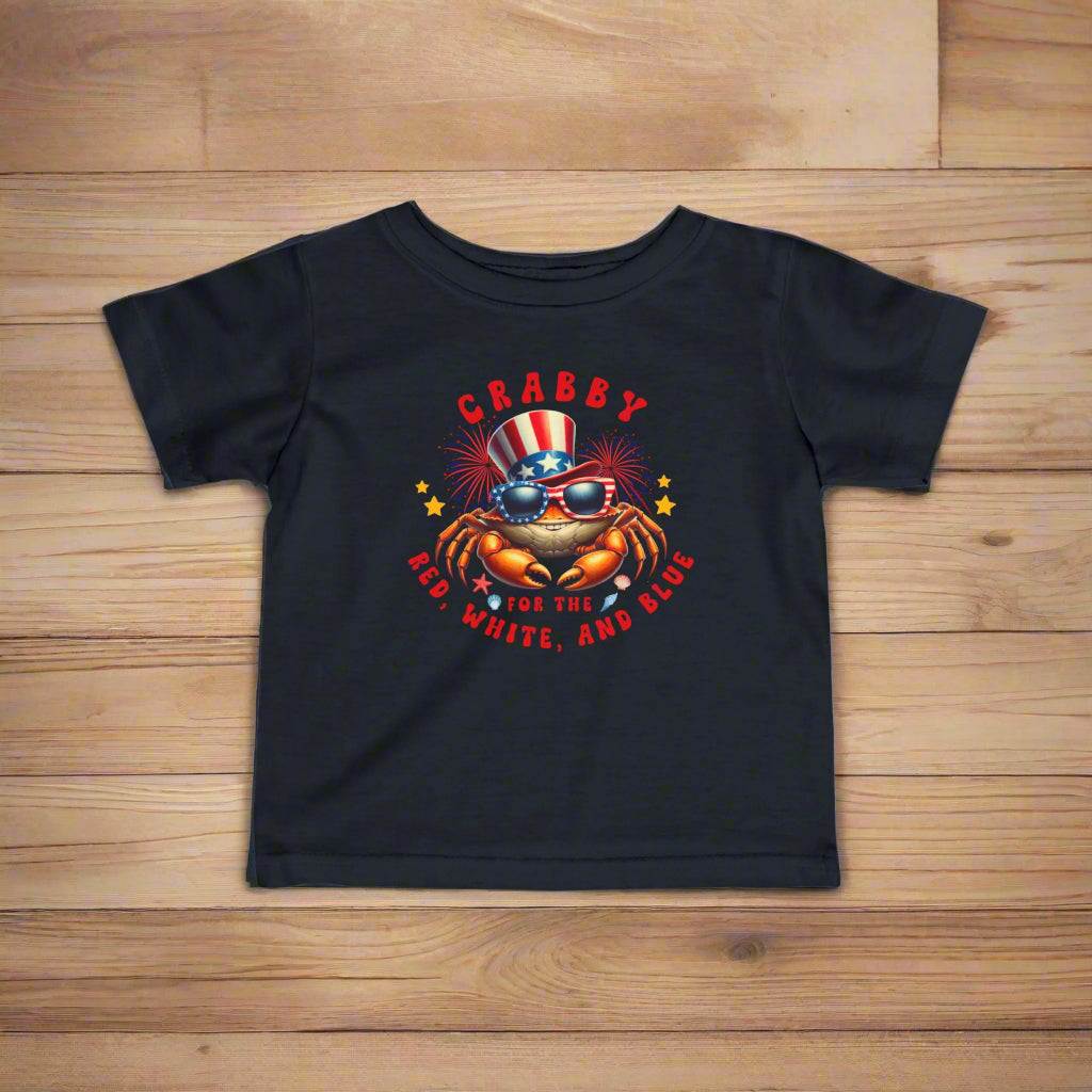 Black Infant t-shirt with a crab wearing an American flag top hat surrounded by fireworks and seashells with the phrase “Crabby for the Red, White, and Blue.”