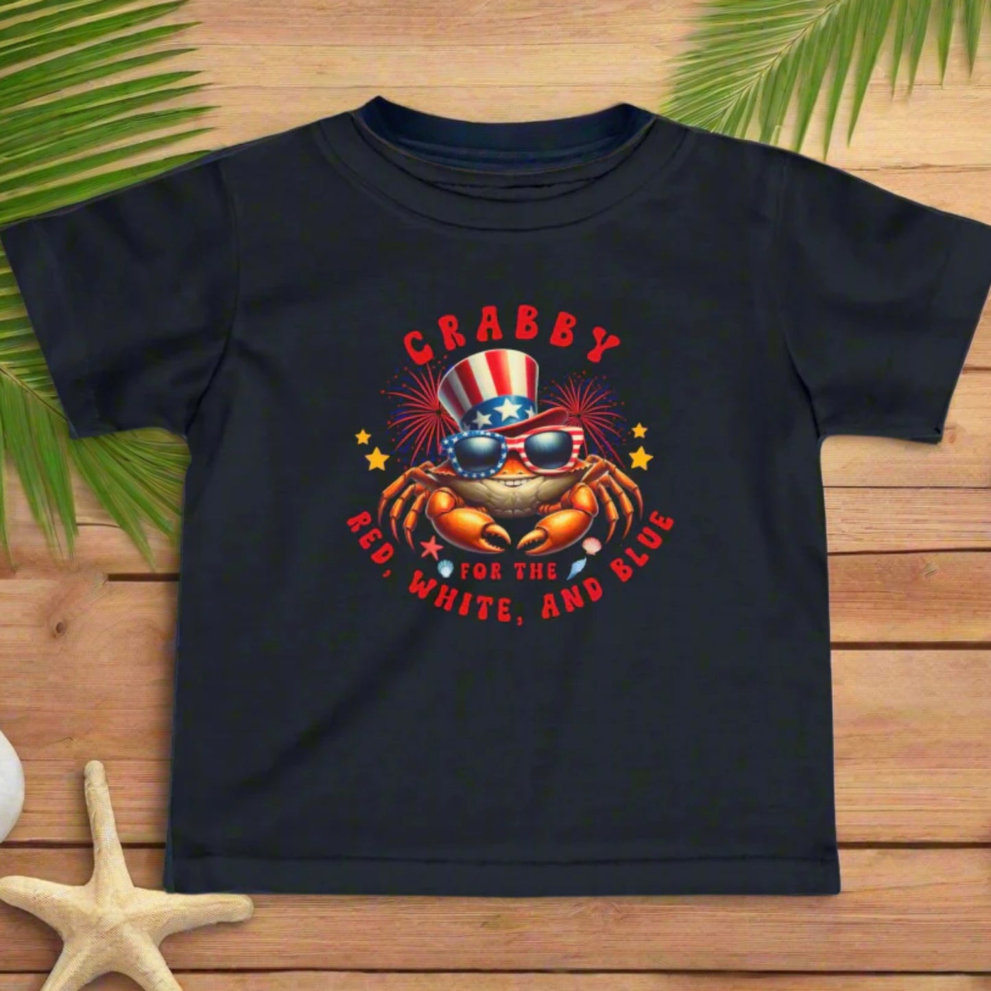 Black Infant t-shirt with a crab wearing an American flag top hat surrounded by fireworks and seashells with the phrase “Crabby for the Red, White, and Blue.”