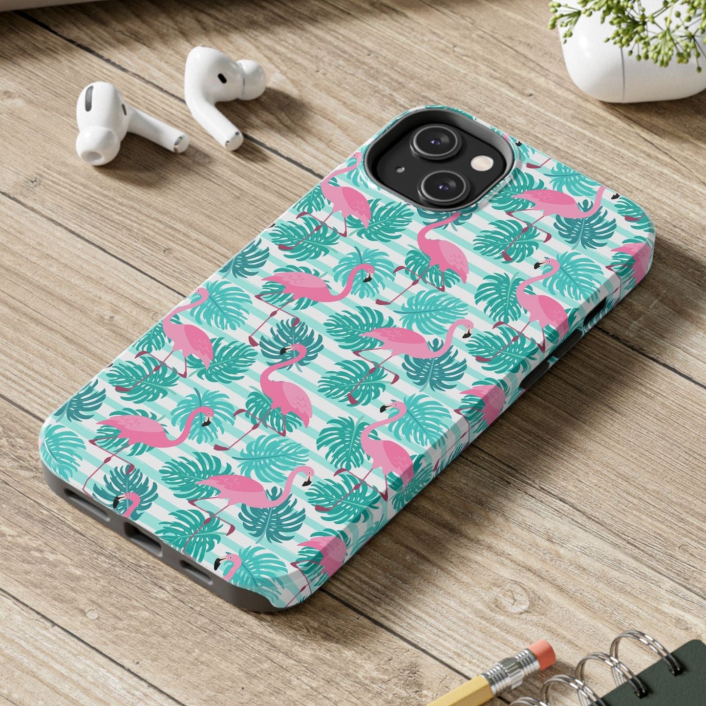 Phone case with flamingo pattern on a wooden surface with laptop, earbuds, and notebook.