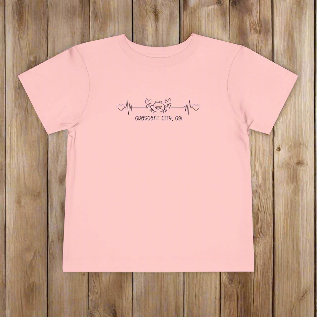 Pink Toddler t-shirt featuring a smiley crab on a heartbeat line with hearts at both ends and the text “Crescent City, CA” underneath.