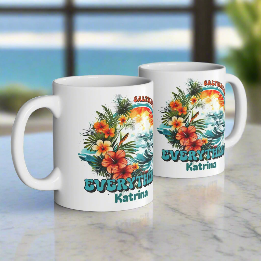 Two white mugs with tropical designs and text on a wooden surface.
