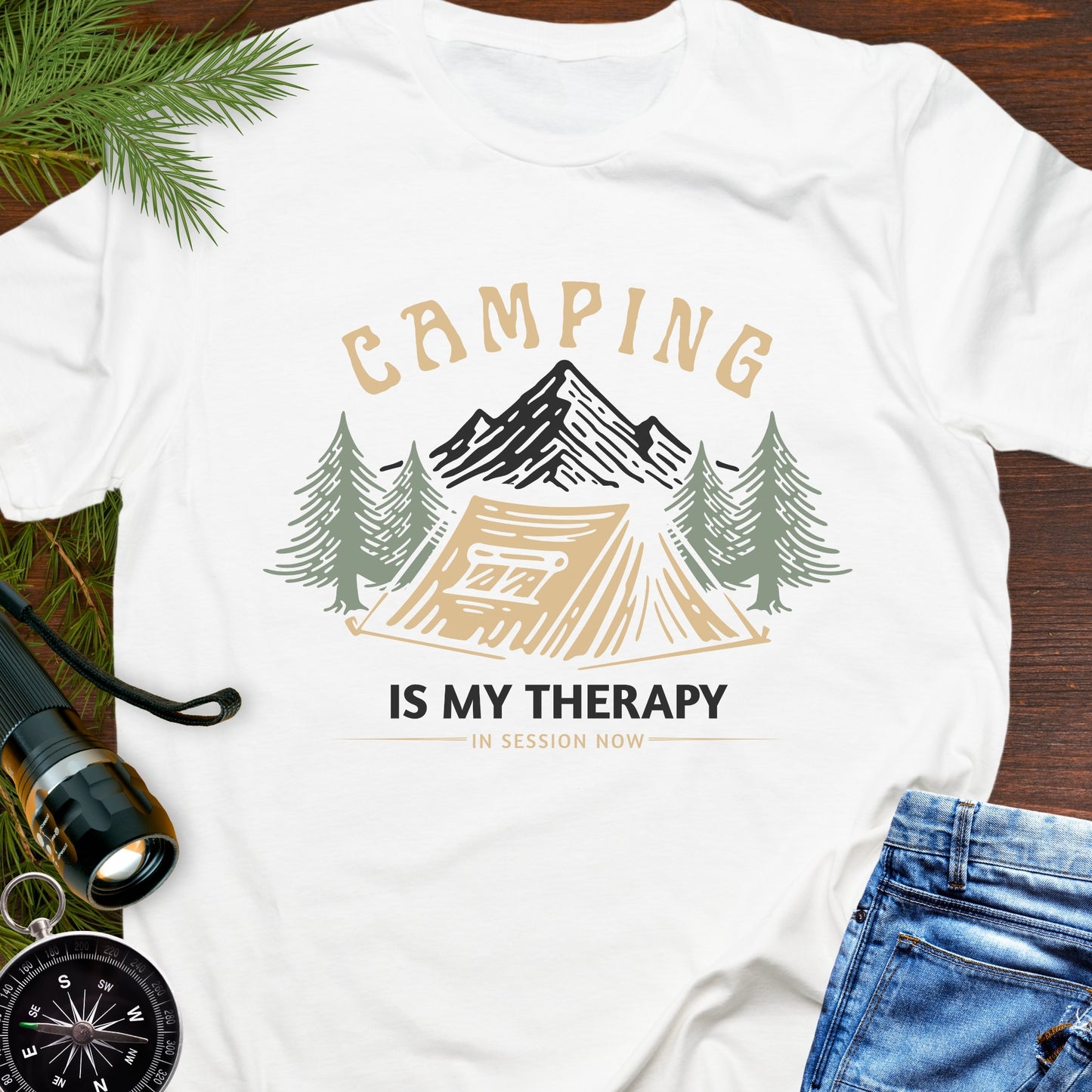 White t-shirt with camping is my therapy text with camping graphic on a wooden surface with accessories.
