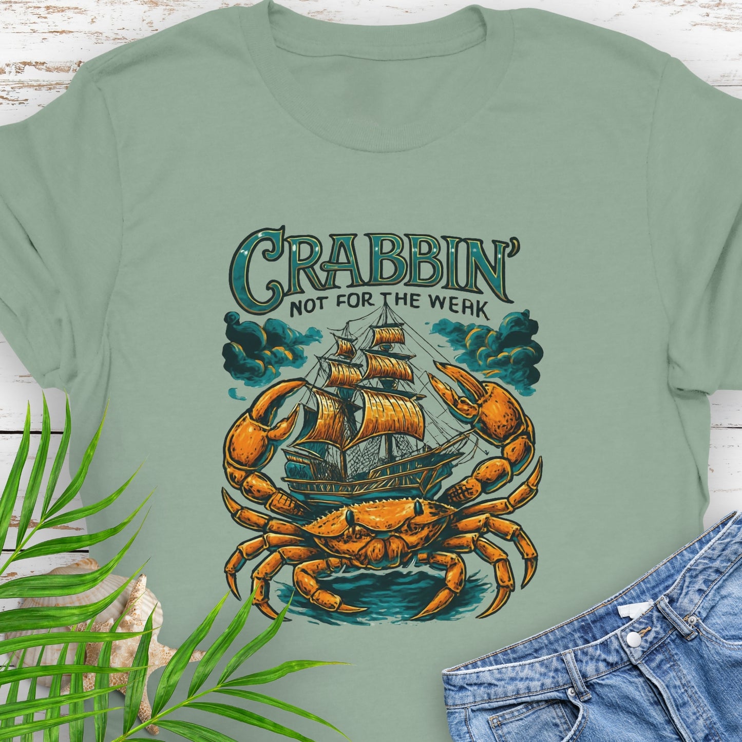 Green t-shirt with a large crab enveloping a pirate ship with the text “Crabbin’s Not for the Weak” in an old-style font.