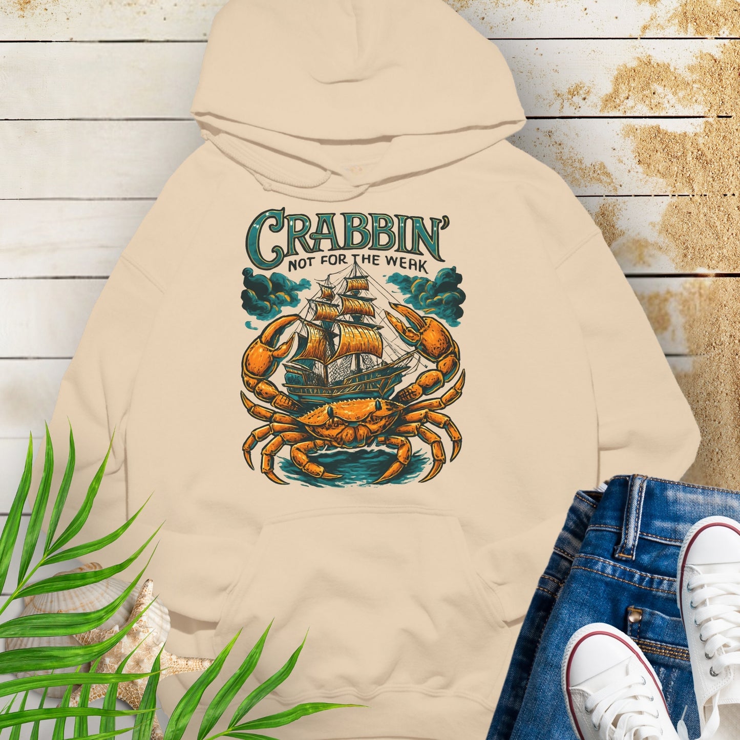 Sand colored hoodie with a large crab enveloping a pirate ship with the text “Crabbin’s Not for the Weak” in an old-style font.