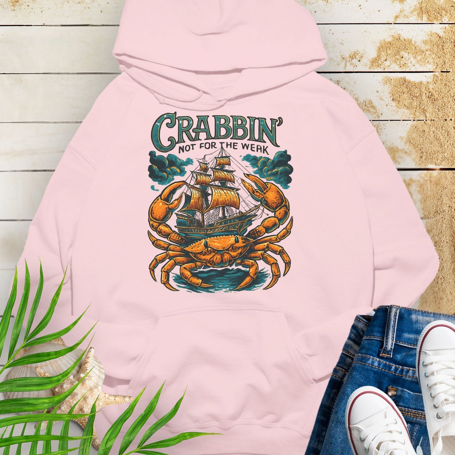 Pink hoodie with a large crab enveloping a pirate ship with the text “Crabbin’s Not for the Weak” in an old-style font.