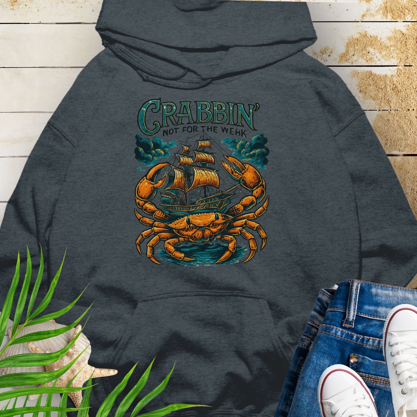 Dark heather gray hoodie with a large crab enveloping a pirate ship with the text “Crabbin’s Not for the Weak” in an old-style font.