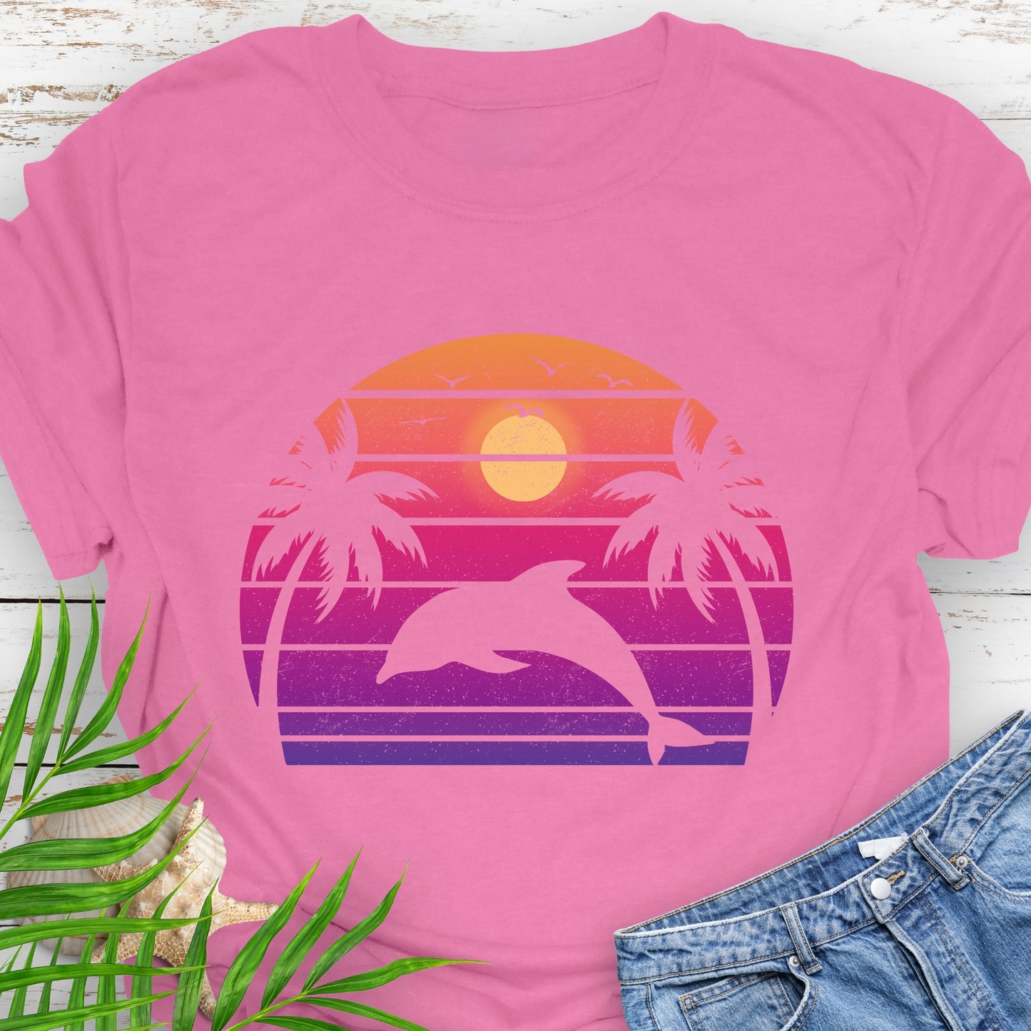 Pink T-shirt with a dolphin against a retro sunset and two palm trees.
