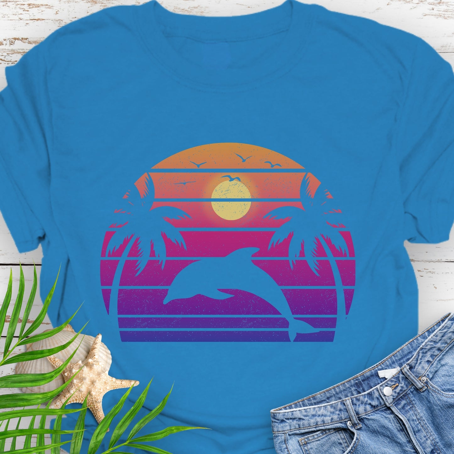 Sapphire Blue T-shirt with a dolphin against a retro sunset and two palm trees.
