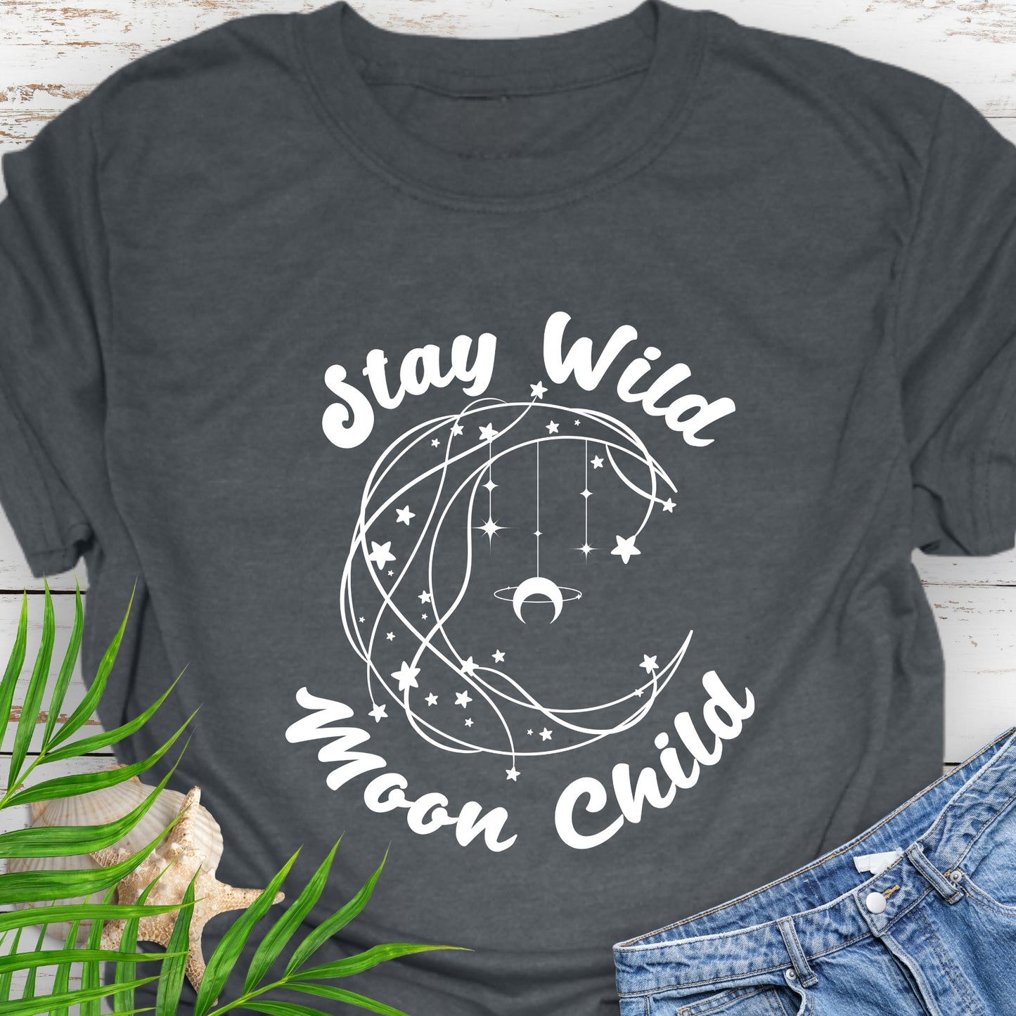 Dark gray T-shirt with crescent shaped lines and hanging crescent moon and stars that says Stay Wild Moon Child.