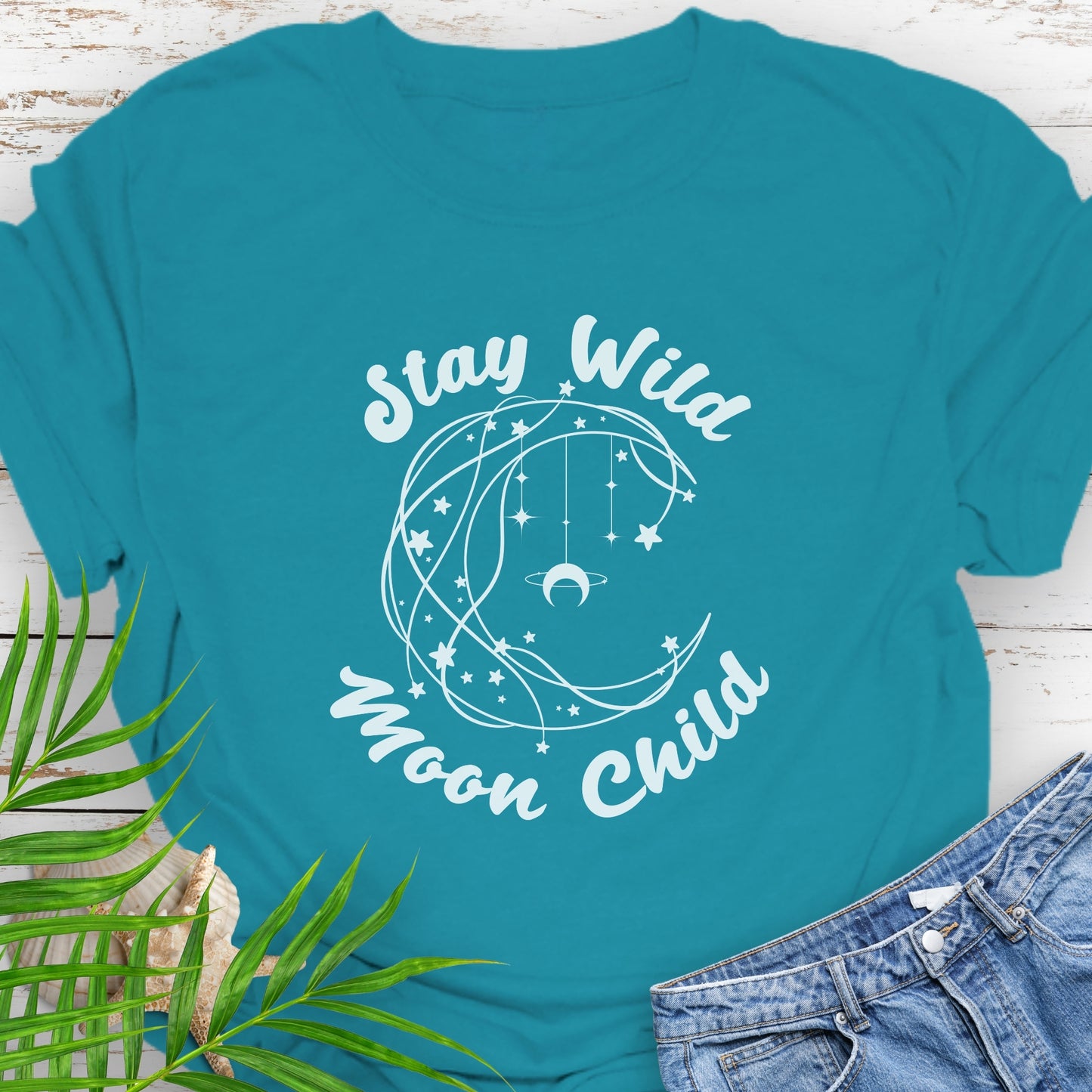 Sapphire Blue T-shirt with crescent shaped lines and hanging crescent moon and stars that says Stay Wild Moon Child.