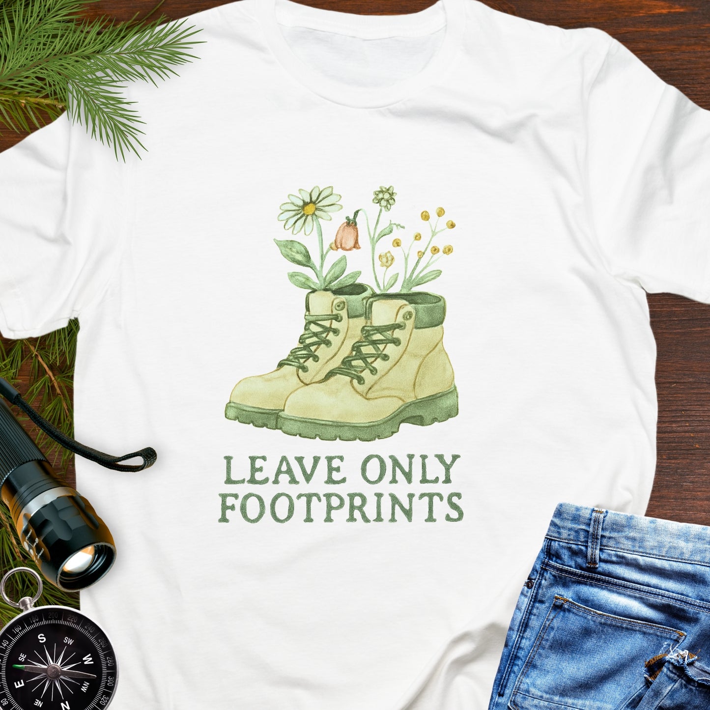White T-shirt with hiking boots and wildflowers that says "Leave Only Footprints."