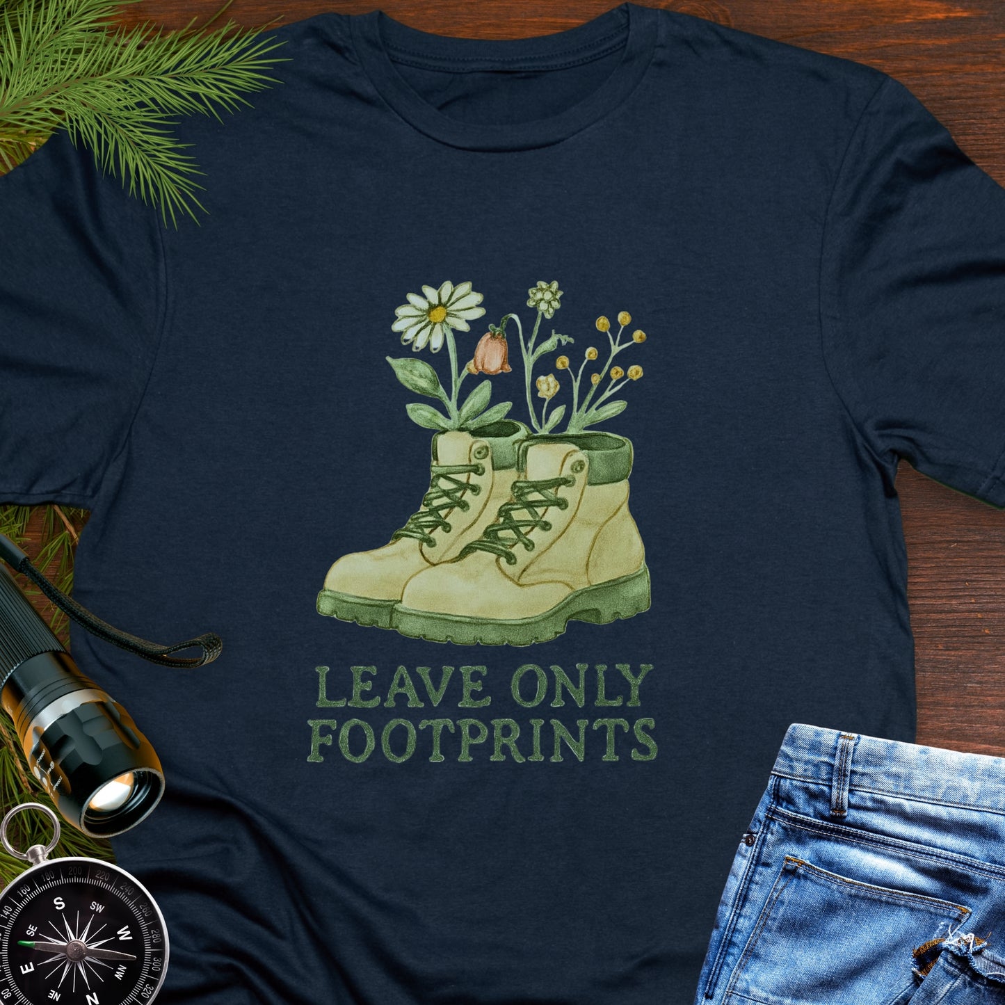 Navy T-shirt with hiking boots and wildflowers that says "Leave Only Footprints."