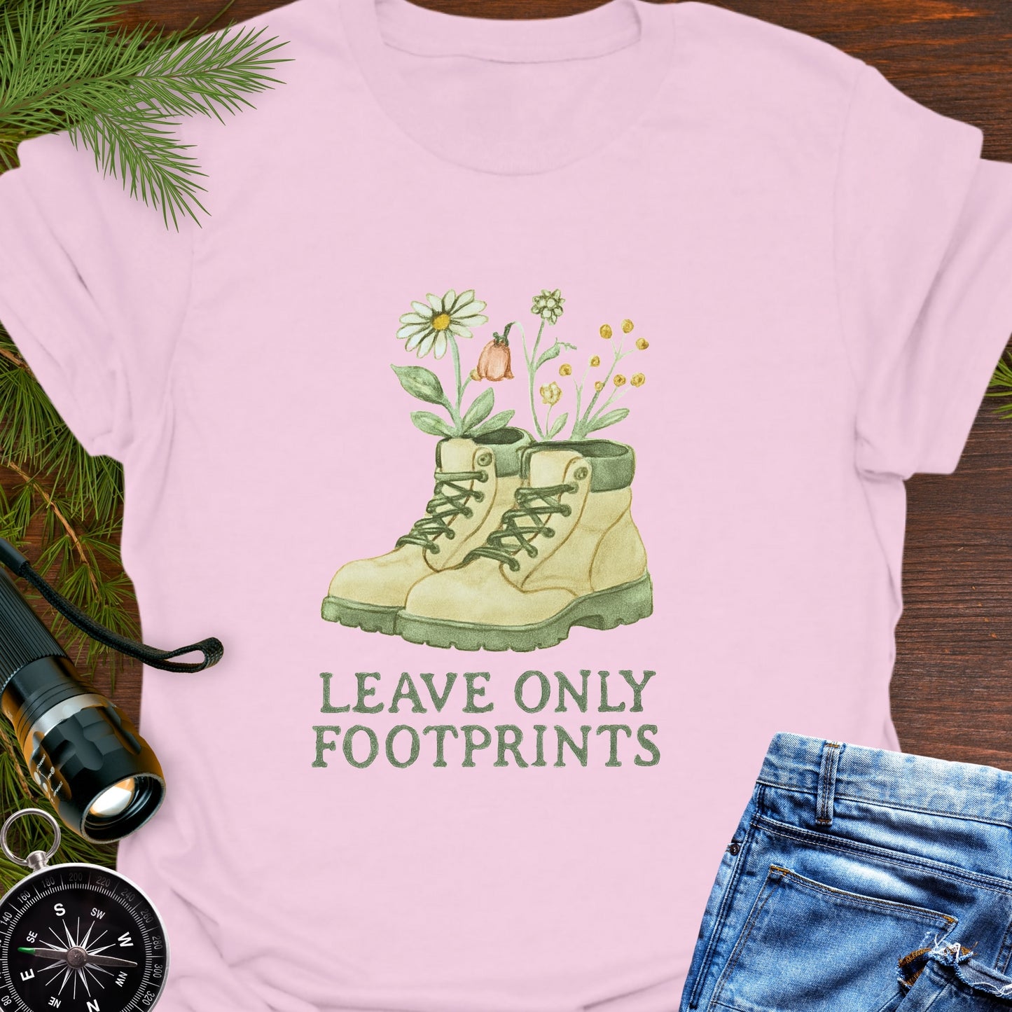 Pink T-shirt with hiking boots and wildflowers that says "Leave Only Footprints."
