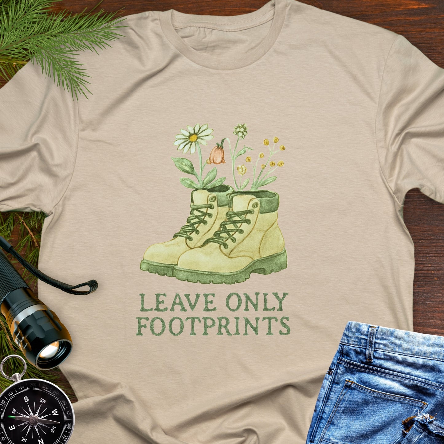 Beige T-shirt with hiking boots and wildflowers that says "Leave Only Footprints."