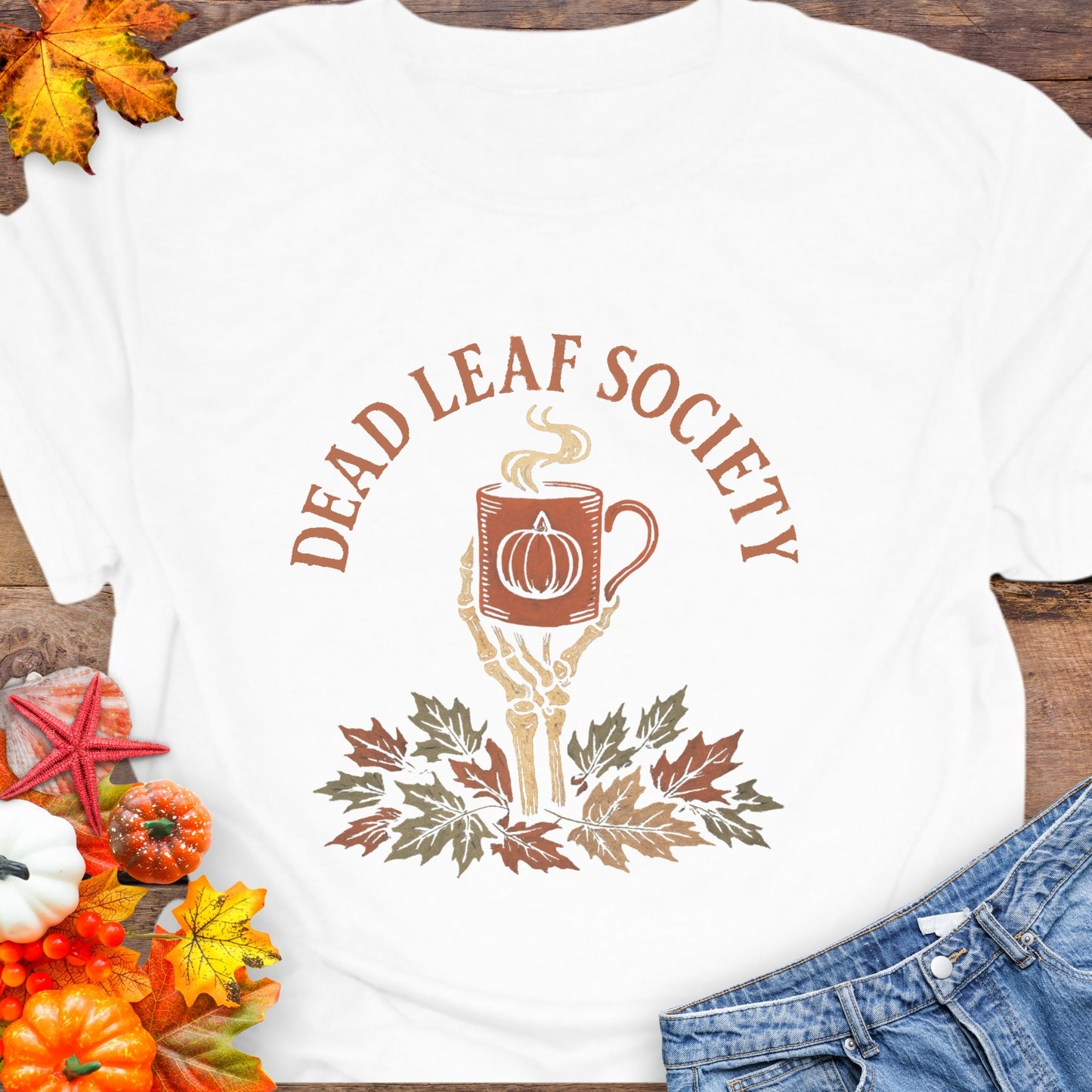 White t-shirt with a skeleton hand holding a coffee cup above fall leaves and the text “Dead Leaf Society.”