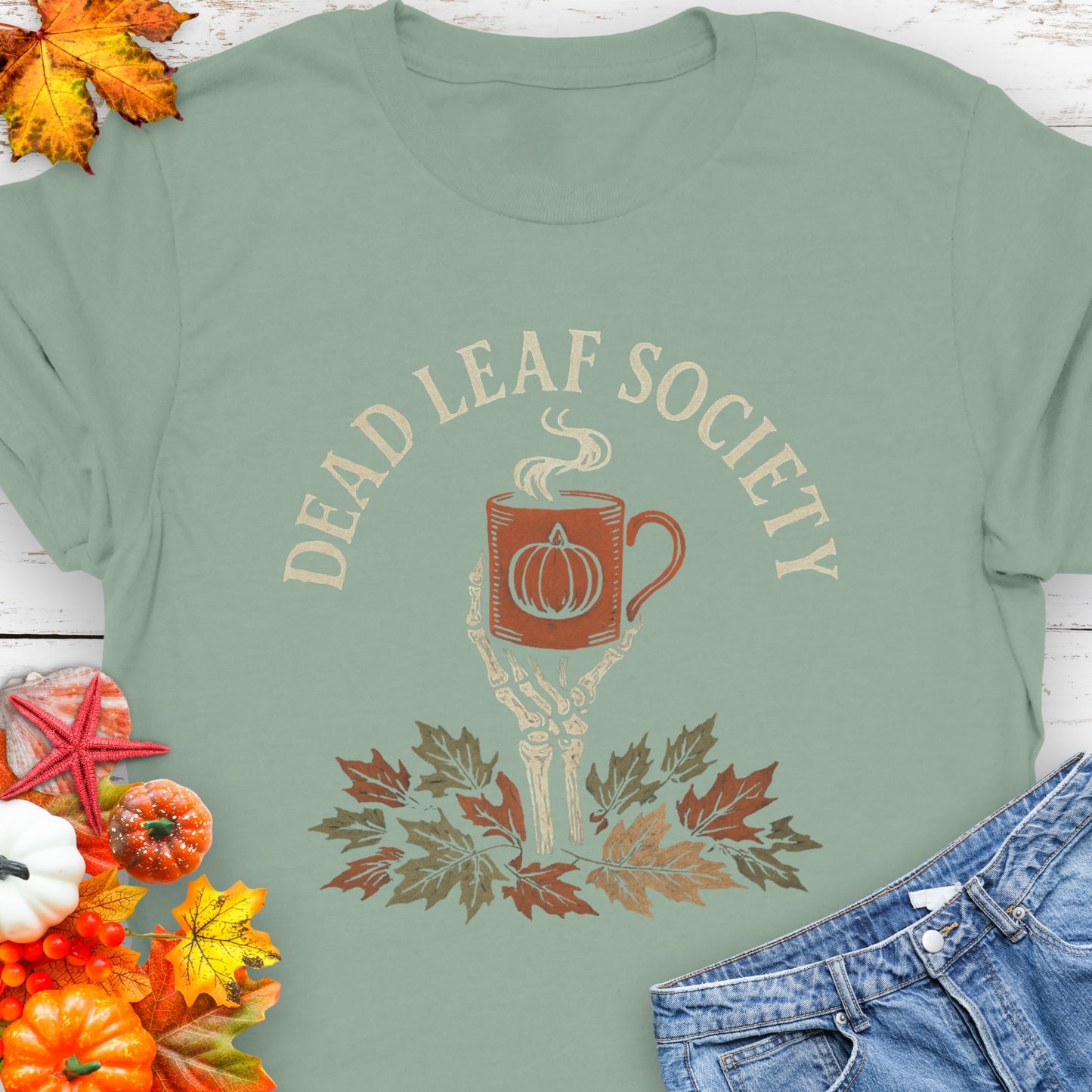 Green t-shirt with a skeleton hand holding a coffee cup above fall leaves and the text “Dead Leaf Society.”