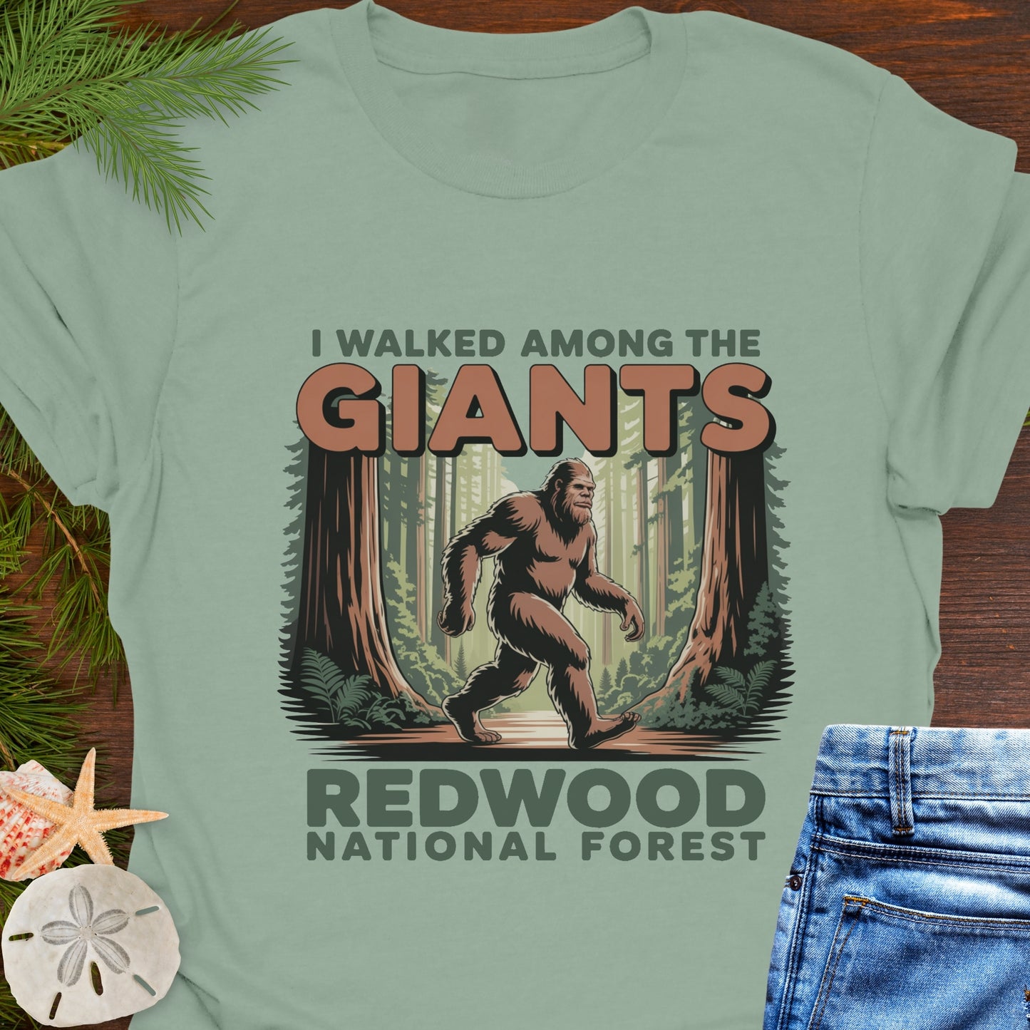 Green t-shirt with Bigfoot graphic and 'Redwood National Forest' text on a wooden surface.