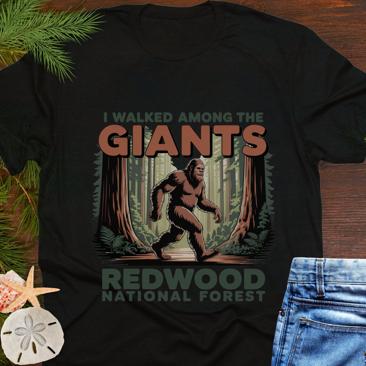 Black t-shirt with Bigfoot graphic and text 'I walked among the giants Redwood National Forest' on a wooden surface.