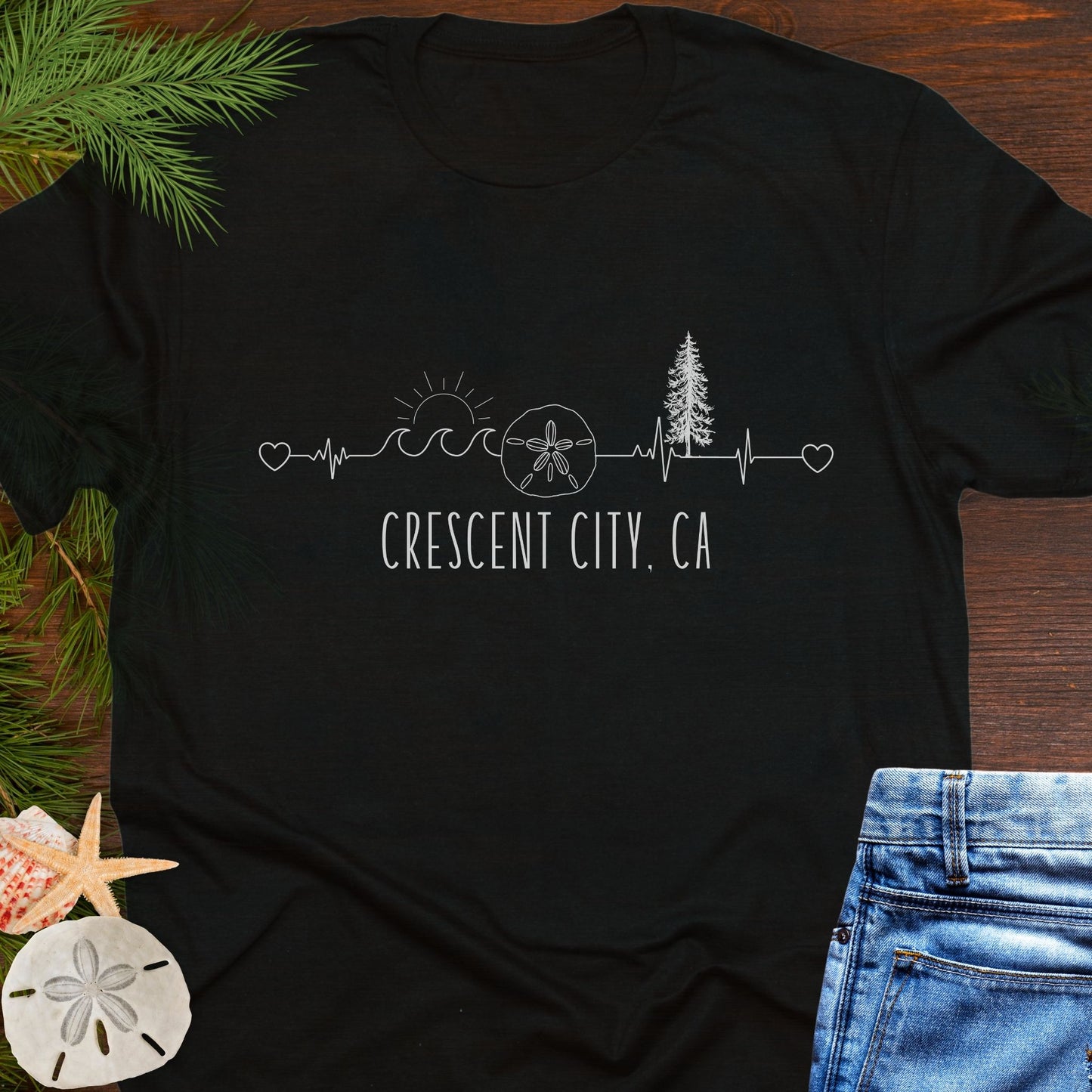 Black t-shirt with white heartline with redwoods, waves, and sand dollar with text 'Crescent City, CA'.