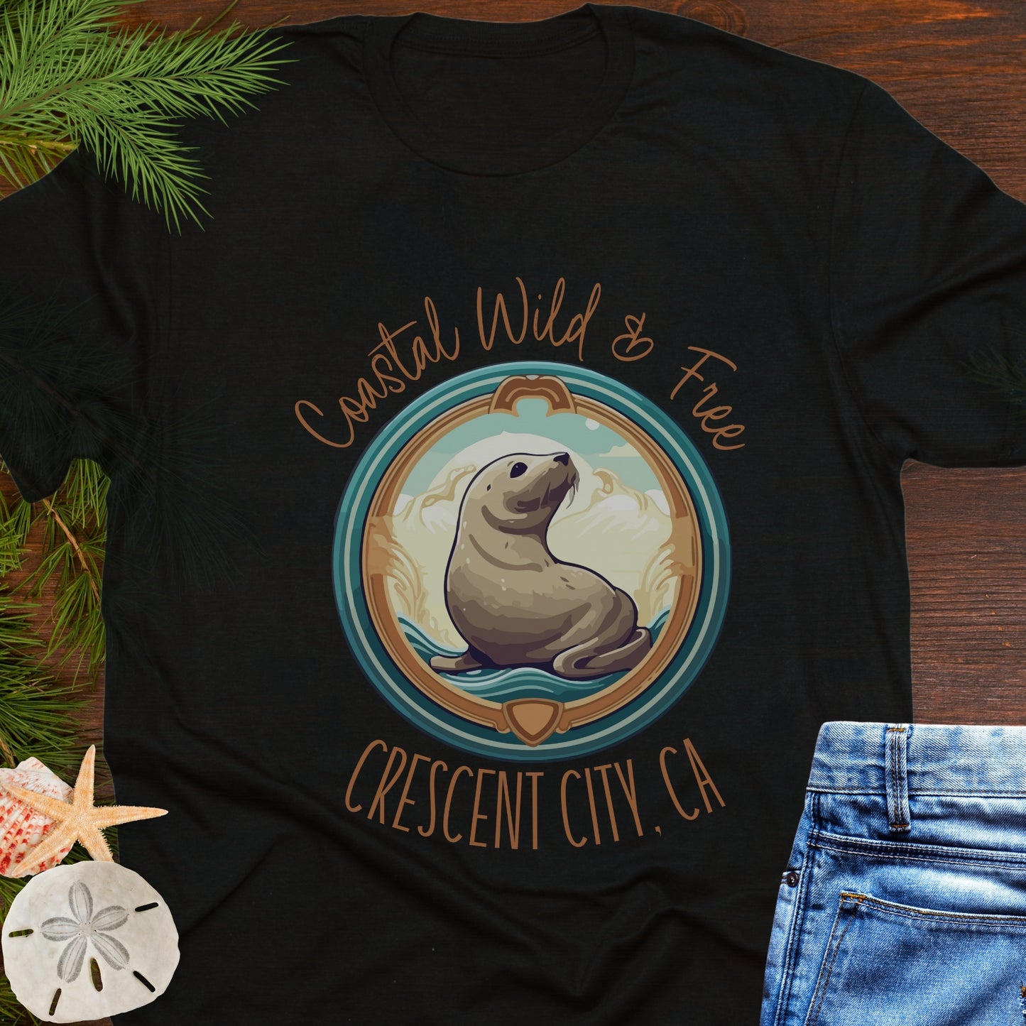 Black t-shirt with a seal graphic and text on a wooden surface with beach-themed items.
