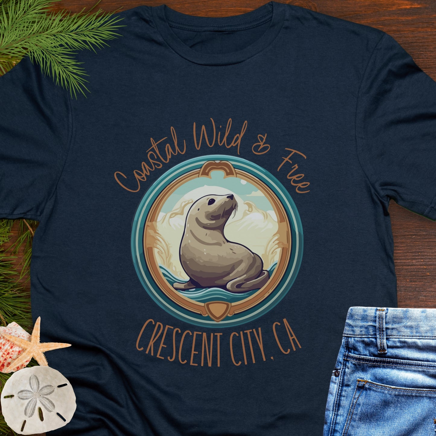 Navy blue t-shirt with a seal graphic and text on a wooden surface with beach-themed items.