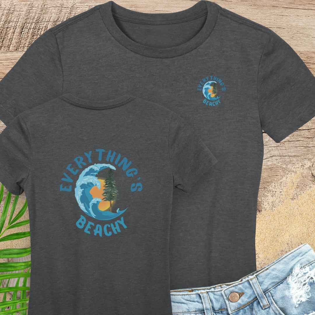 Dark gray t-shirt with 'Everything's Beachy' graphic on a wooden surface with sand and a leaf.