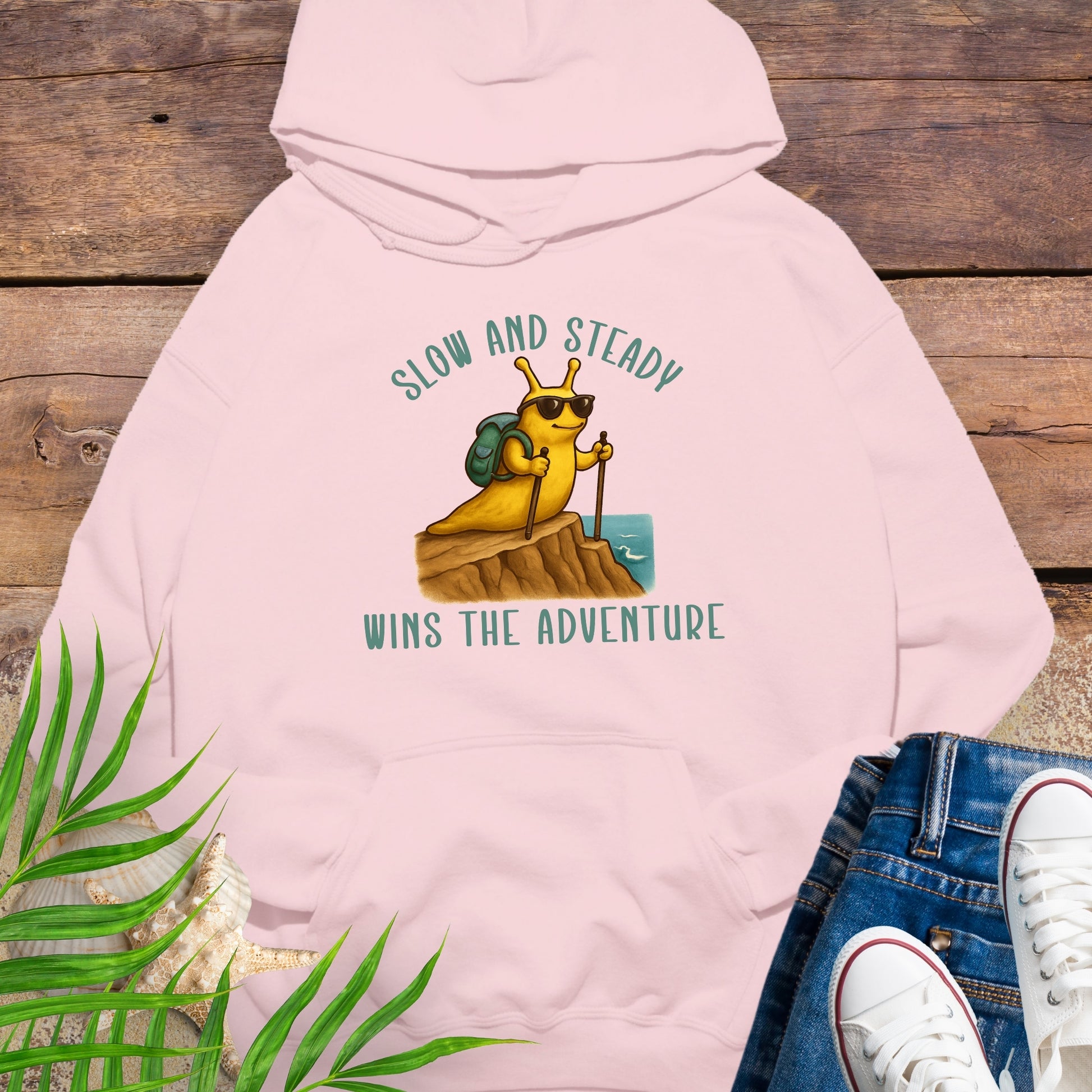 Pink hoodie with a cartoon bear and text 'Slow and Steady Wins the Adventure' on a wooden surface.