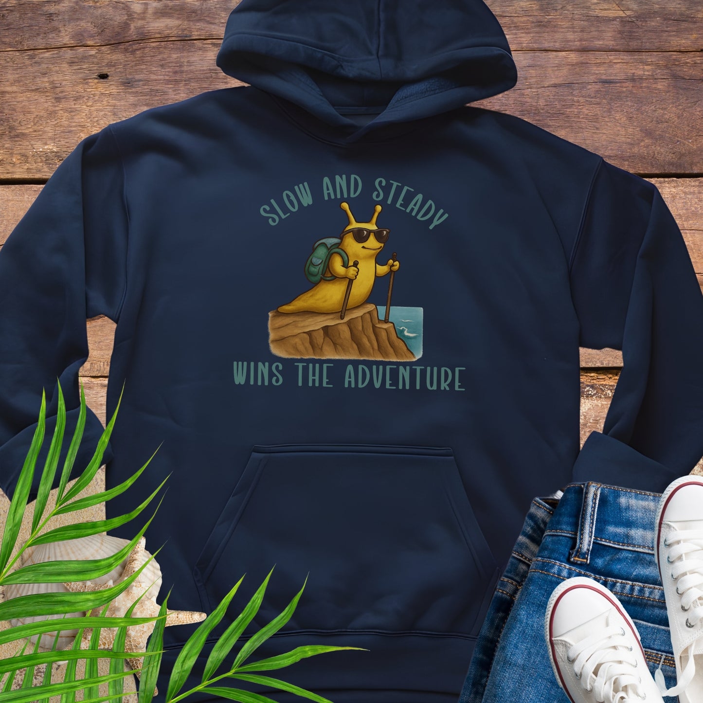 Navy blue hoodie with a cartoon character and text 'Slow and Steady Wins the Adventure' on a wooden surface.