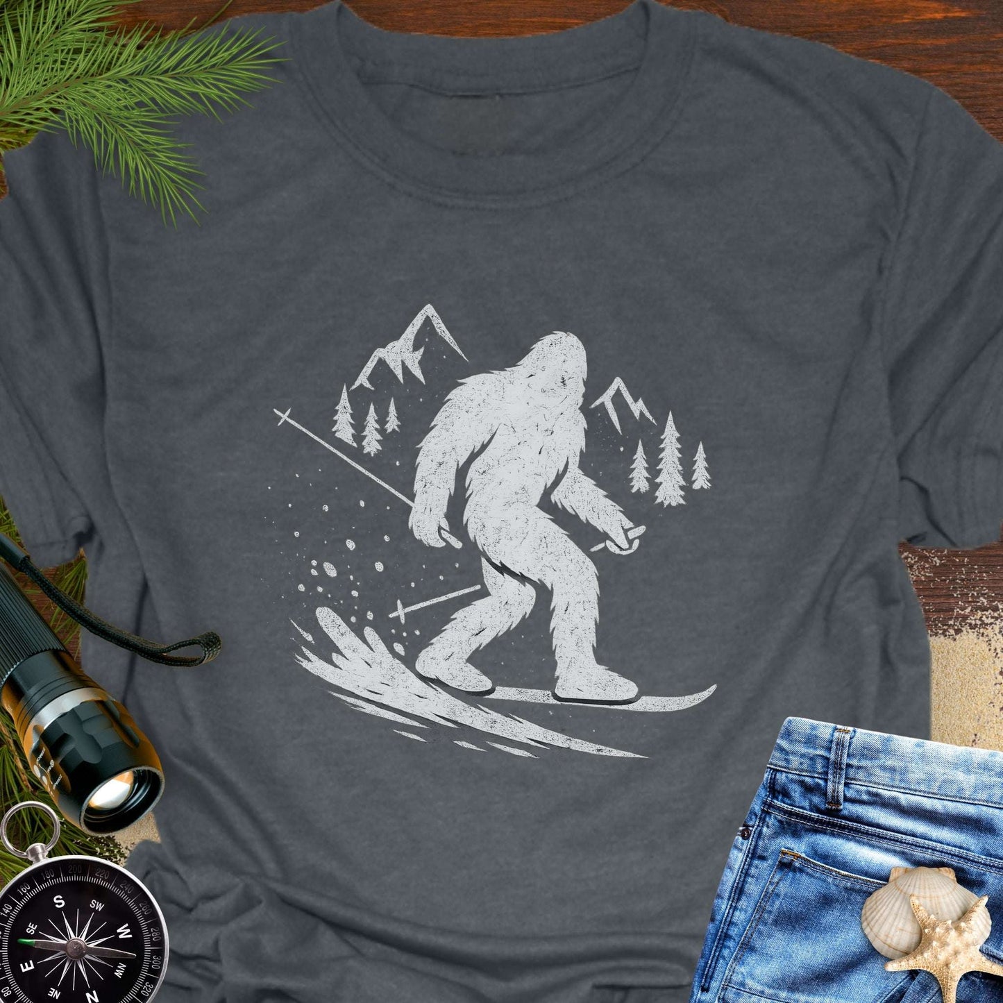 Gray t-shirt with a white graphic of bigfoot skiing down a mountain.