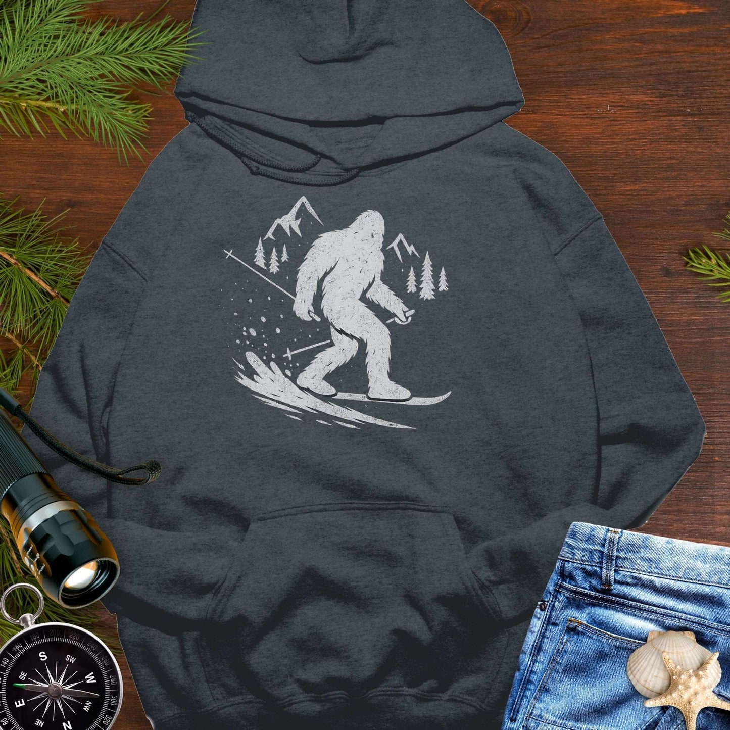Dark gray hoodie with a white graphic of a snowboarding Sasquatch down a mountain.